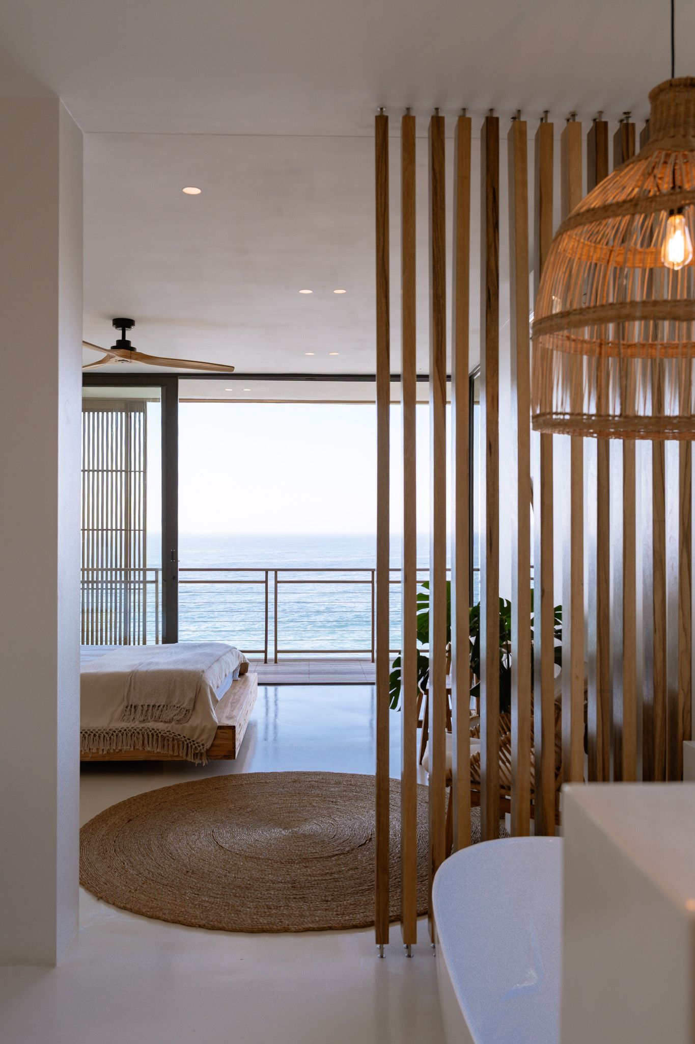 Minimalist bedroom with wooden room divider and natural woven pendant lamp overlooking the sea.