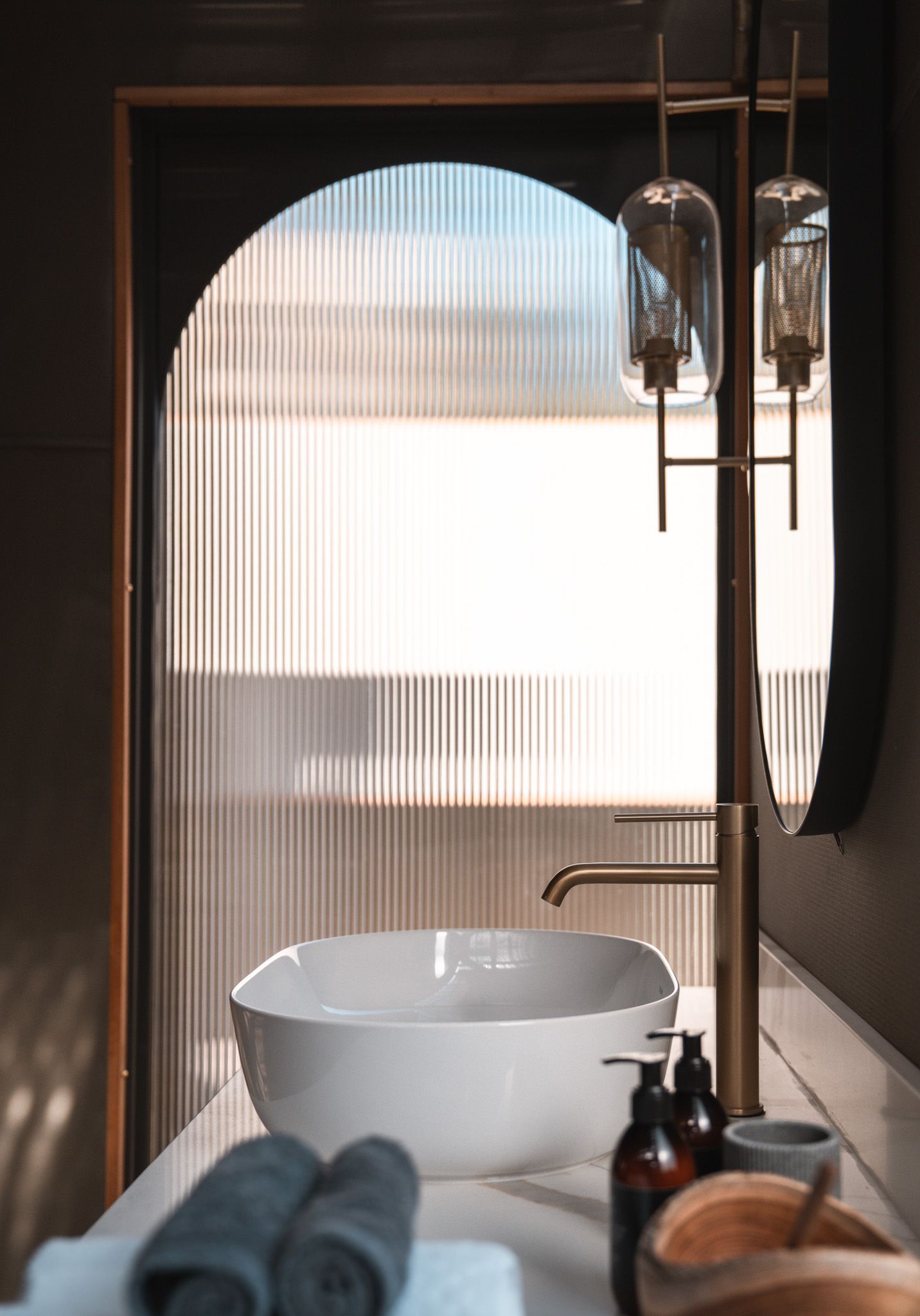 Modern bathroom featuring ribbed glass partition and copper fixtures in soft natural lighting.