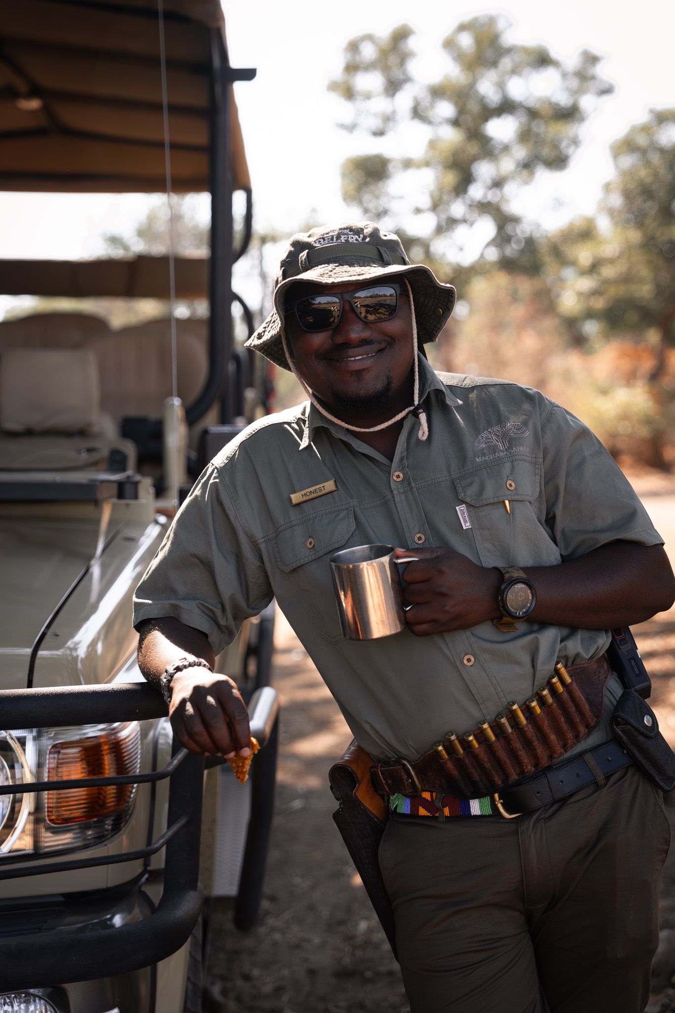 Safari guide in uniform with equipment belt standing next to safari vehicle.