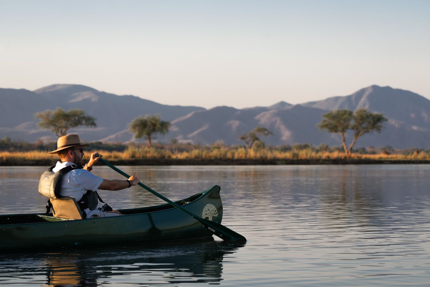 Two people paddling green canoe on serene lake with mountain backdrop.
