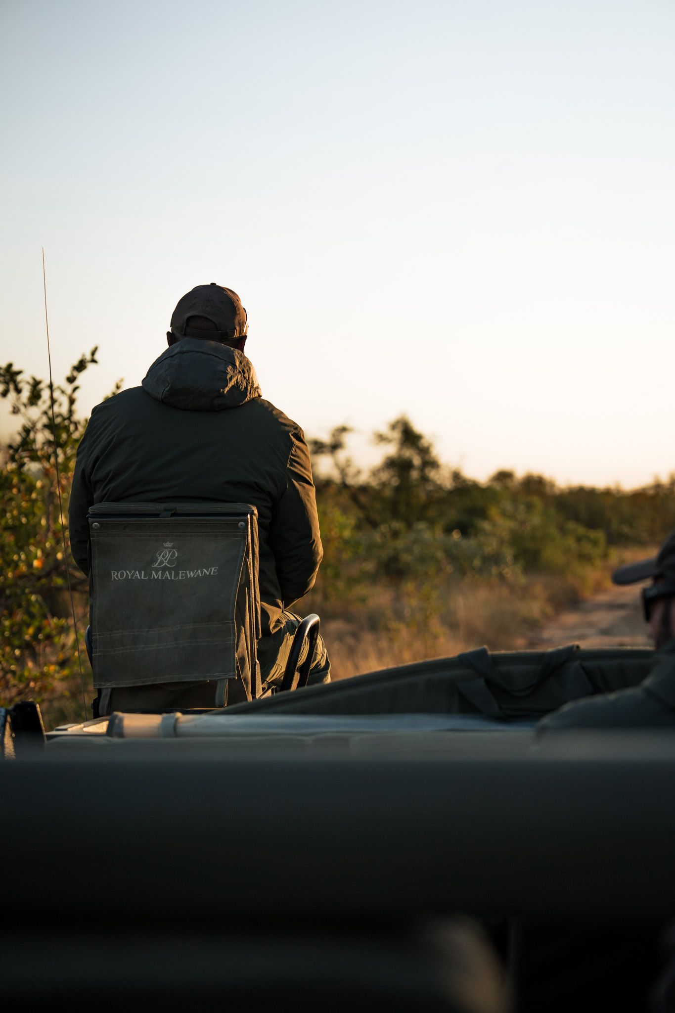 Person sitting on vehicle watching sunset in outdoor adventure setting.