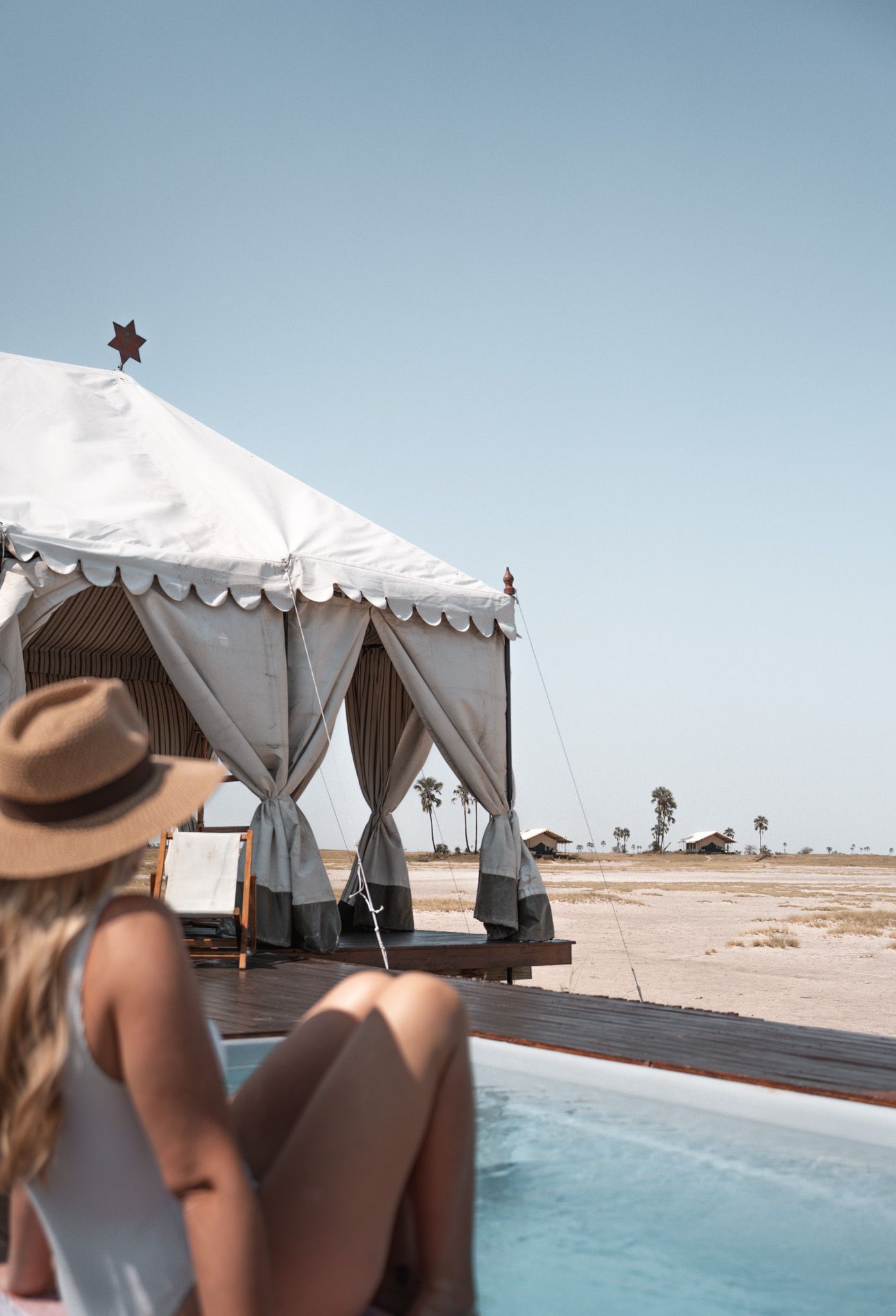 Luxury white safari tents line a swimming pool in a desert landscape under blue skies.