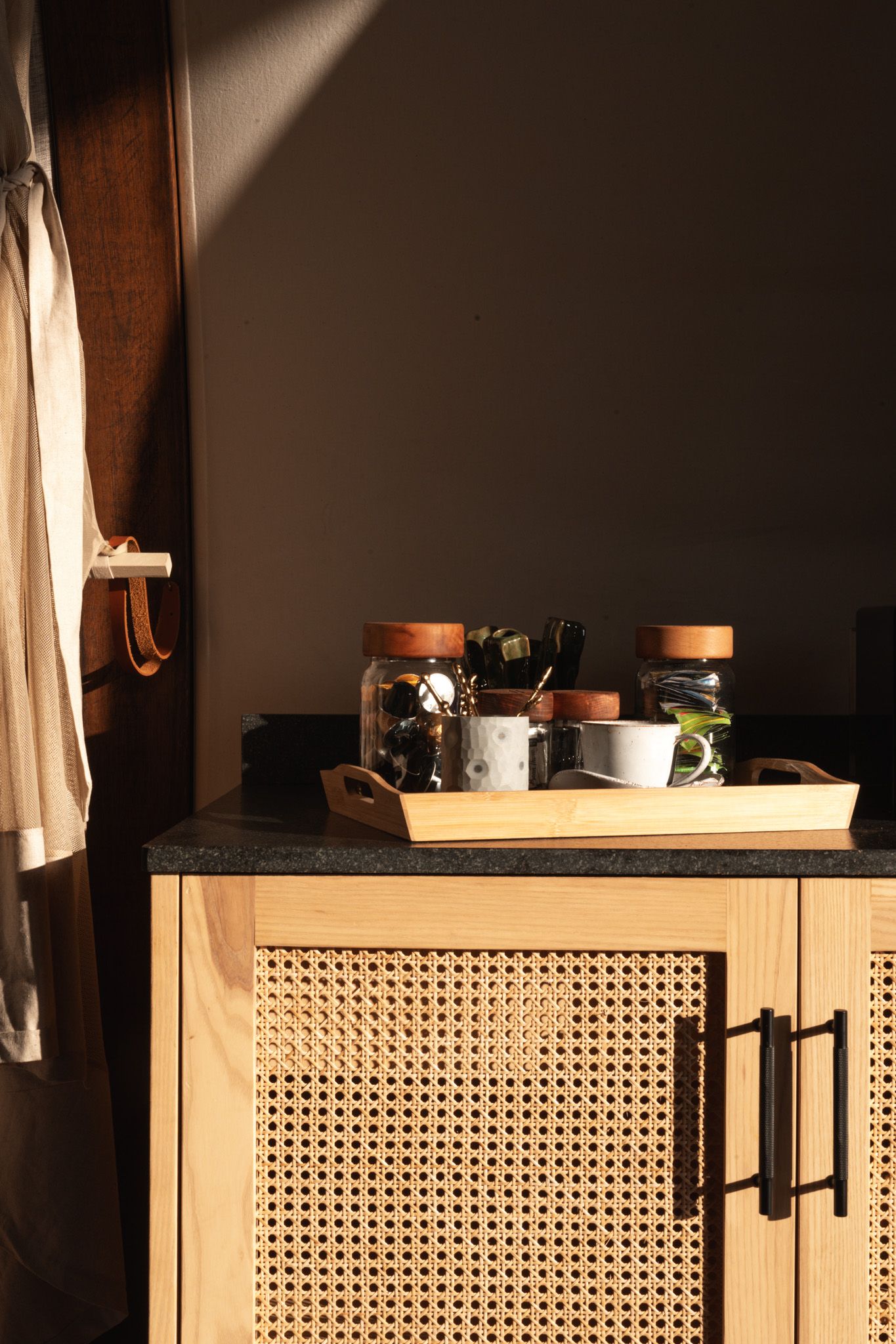 Sunlit wooden cabinet with cane webbing door displaying glass jars on top.