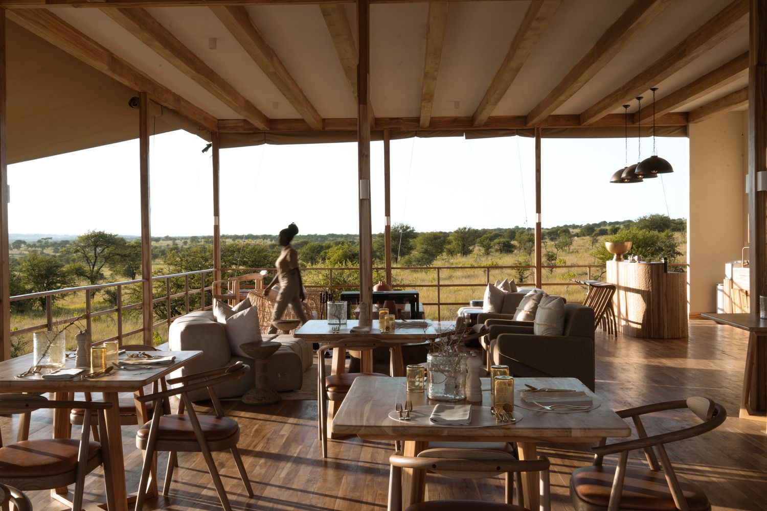 Luxurious safari lodge interior with comfortable seating and panoramic views of African savanna through large windows.