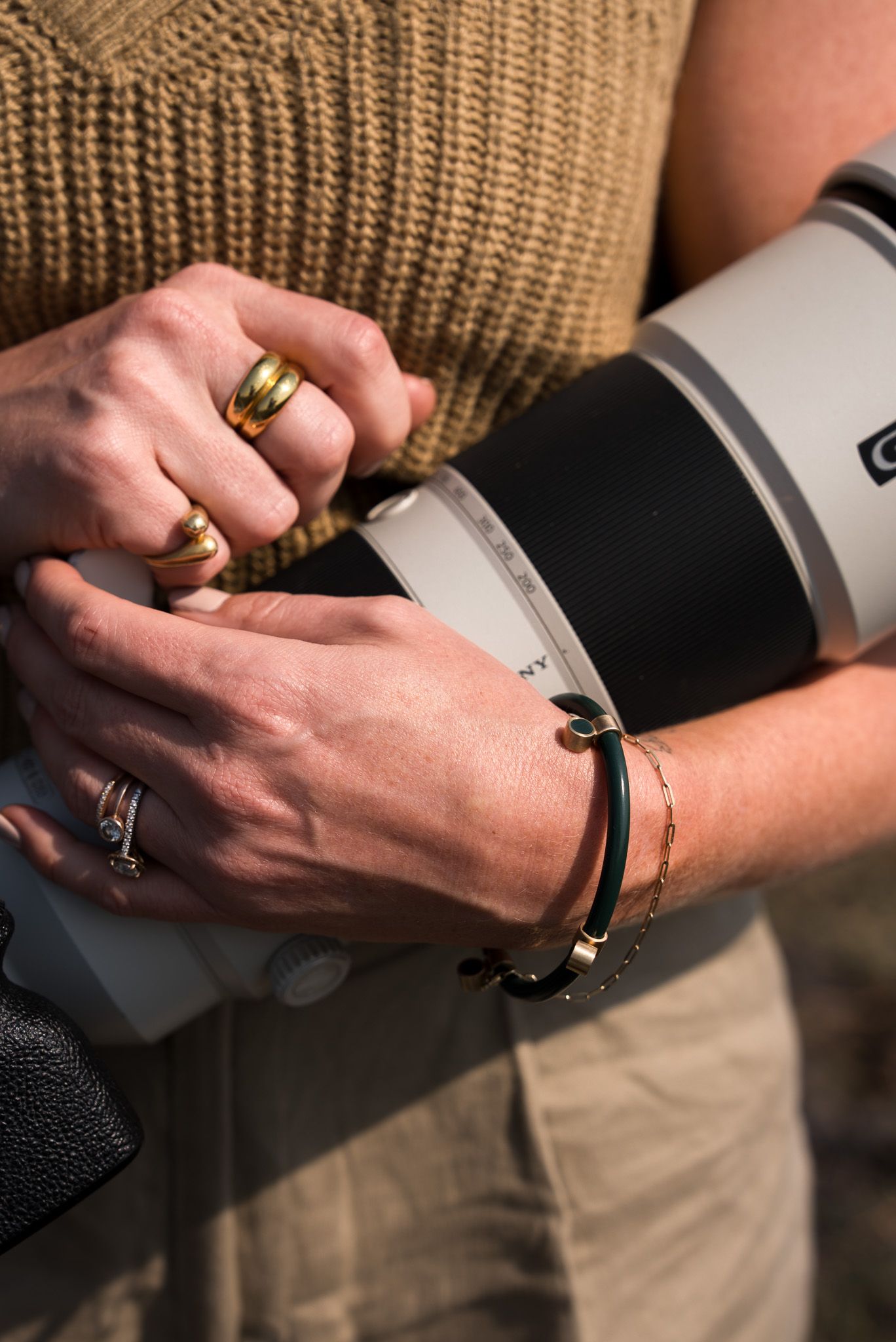 Hands wearing jewelry hold a professional camera lens during a wildlife photo shoot.