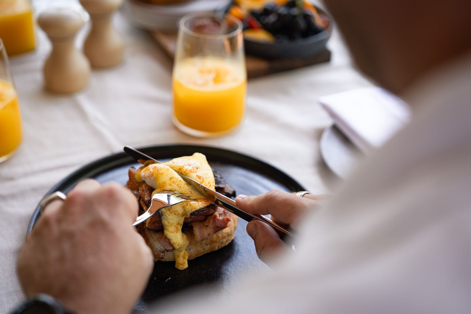 Close-up of hands cutting into breakfast food with orange juice in background.