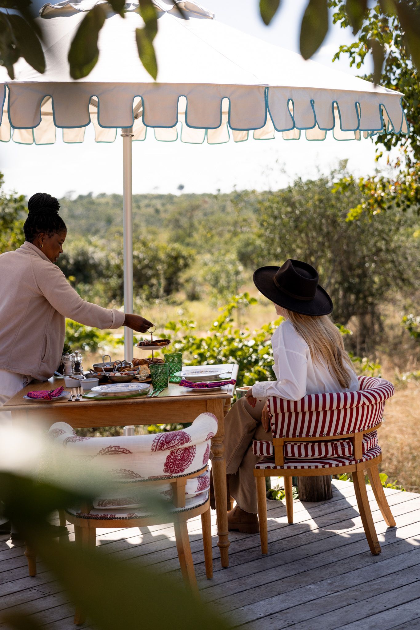 Outdoor dining setup under striped umbrella on wooden deck in safari setting.