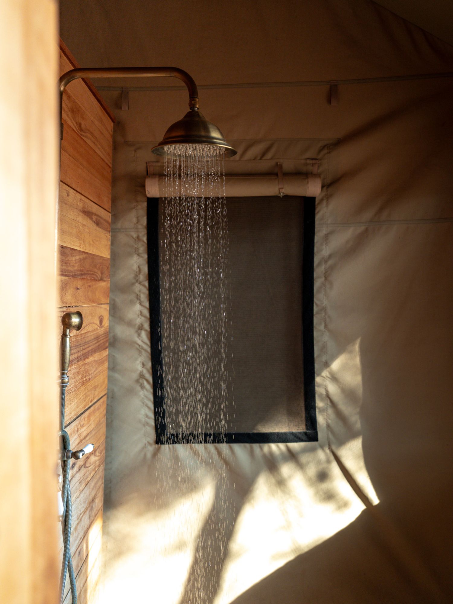 Outdoor shower with running water against wooden wall panels in natural light.