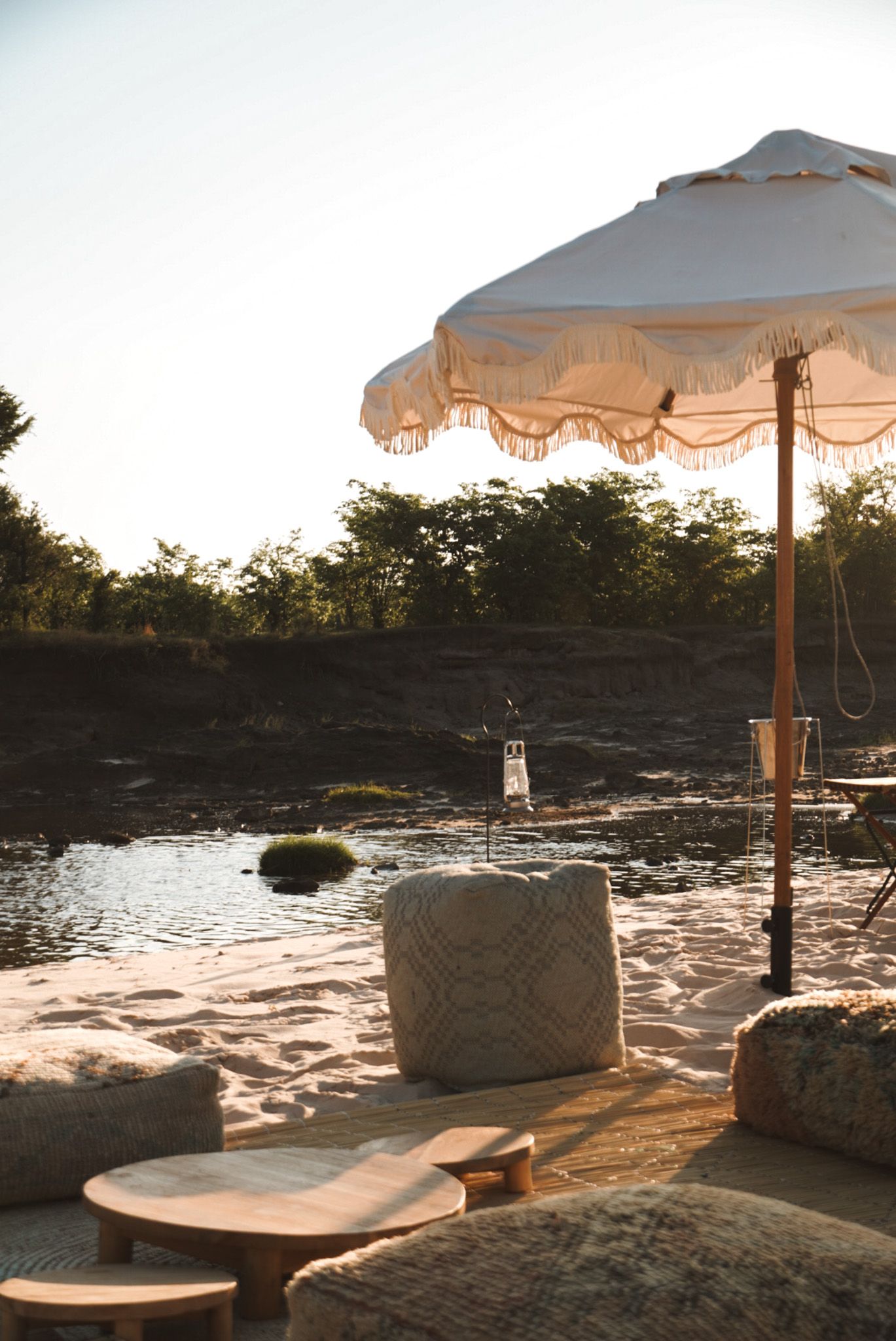 Outdoor lounge area with white umbrellas and stone seating arrangements by the water during sunset.