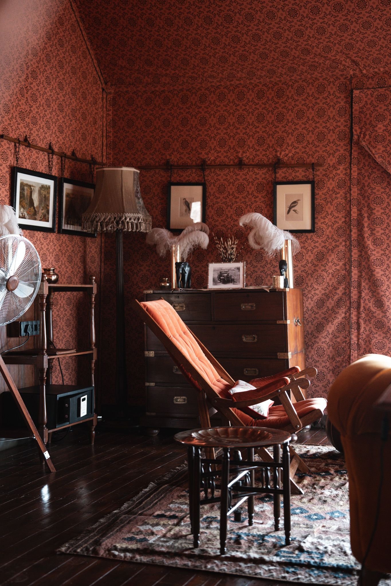 Vintage reading room with red wallpaper, wooden furniture, and framed artwork displaying classic charm.