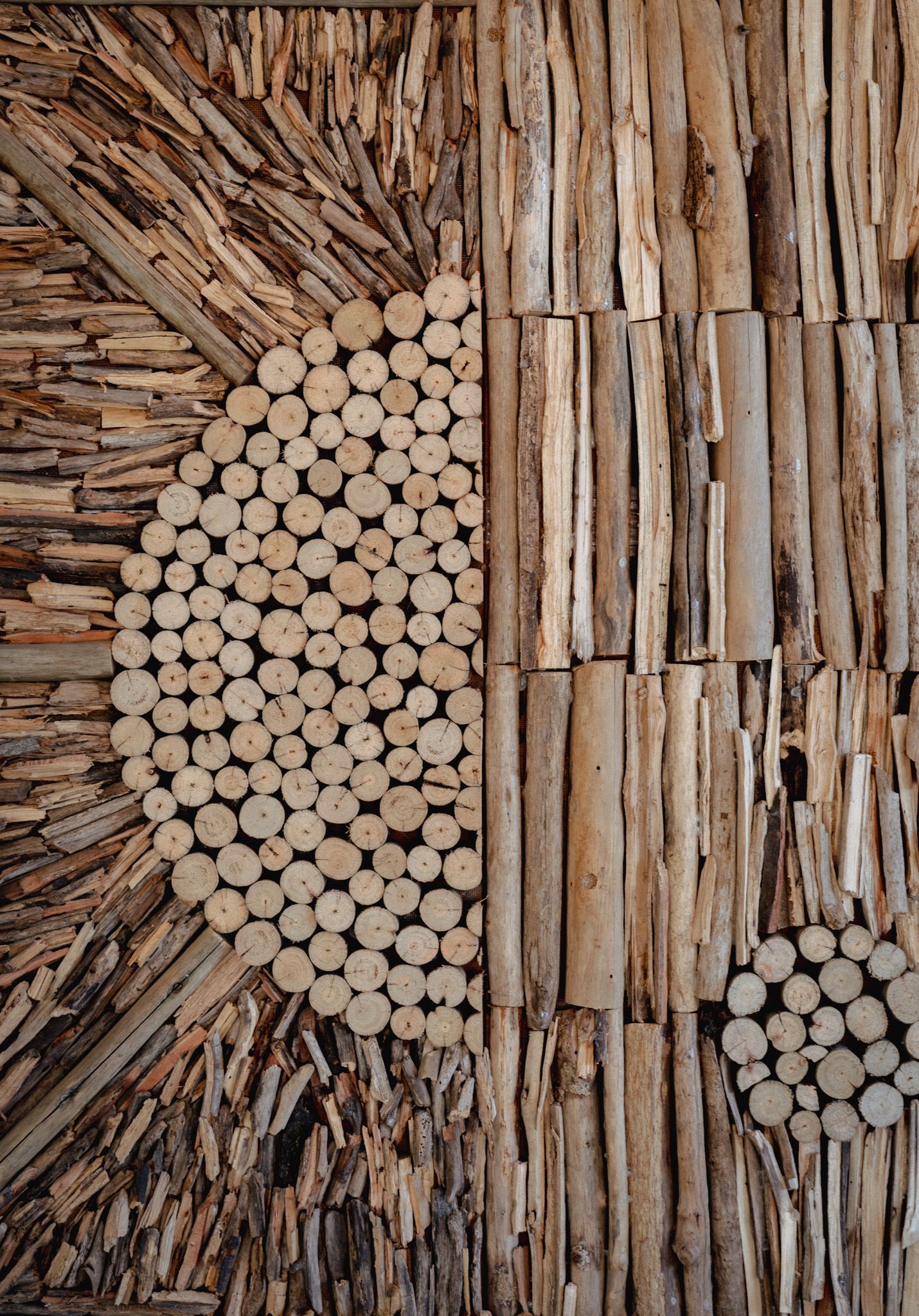 Artistic wall decoration made from arranged wooden sticks and circular log patterns.
