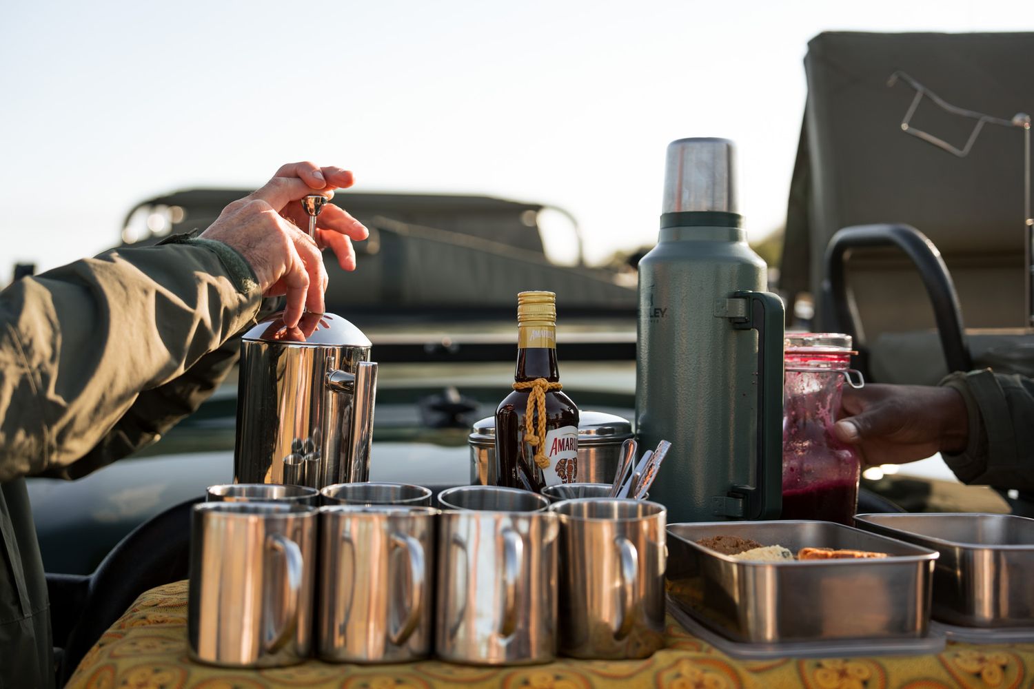 Camping setup with thermos, metal containers and cooking gear arranged on vehicle tailgate.
