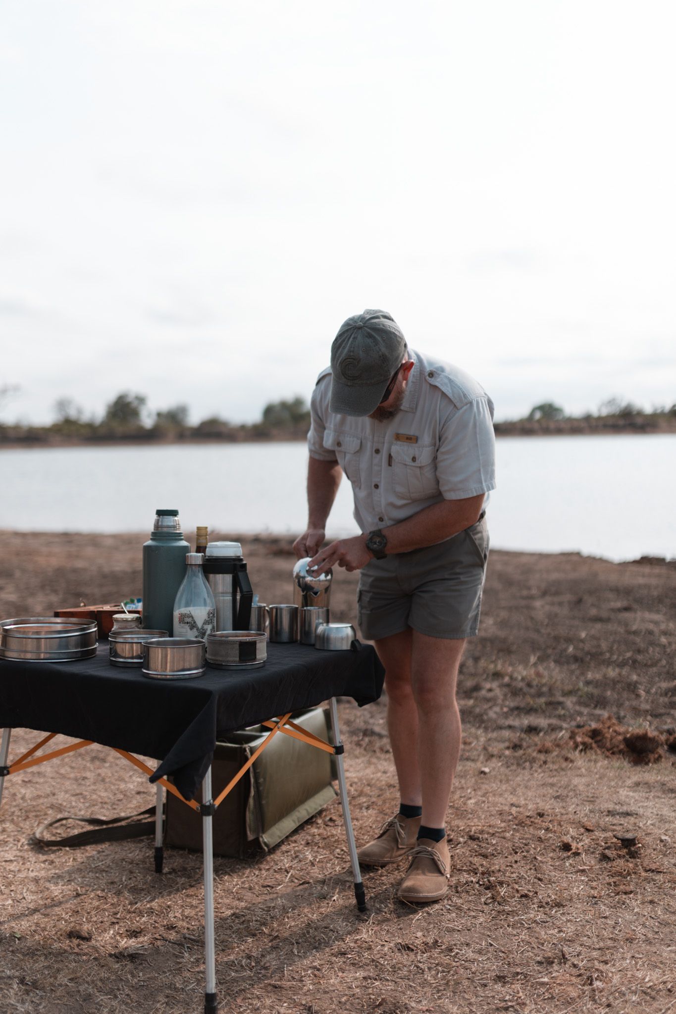 Camping setup with portable stove and cookware by a lake.