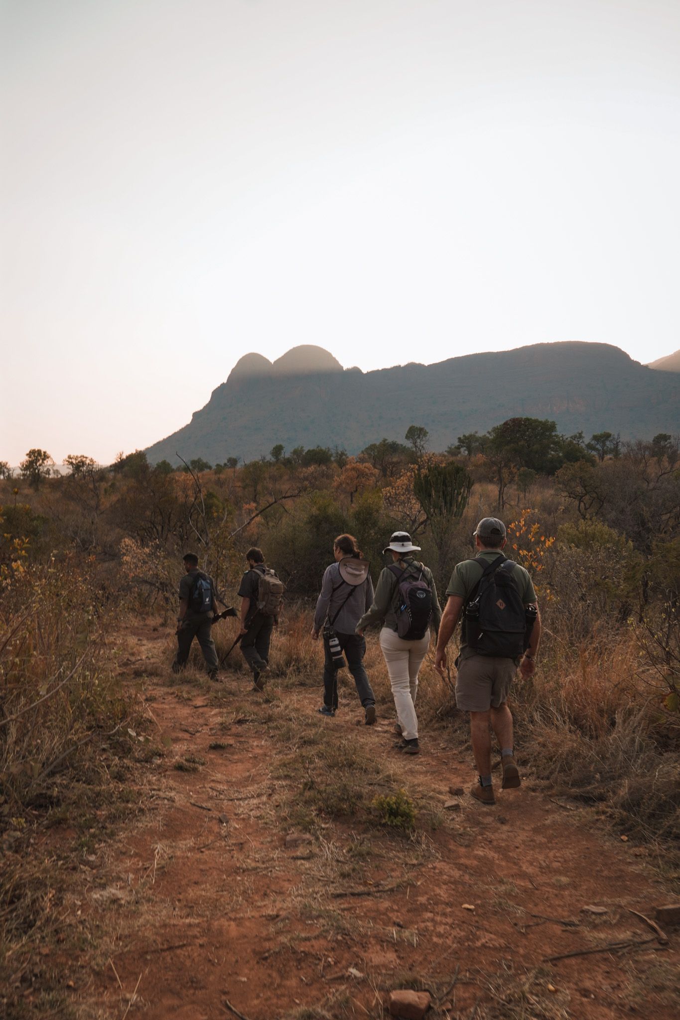 Group of hikers walking along a dusty mountain trail during sunset.