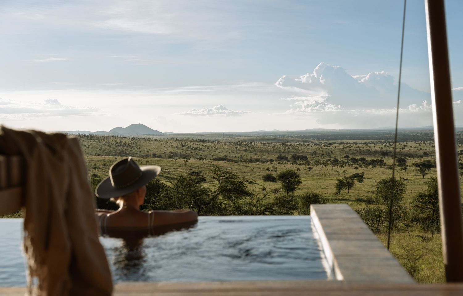 Infinity pool overlooking vast African savanna landscape during sunset.