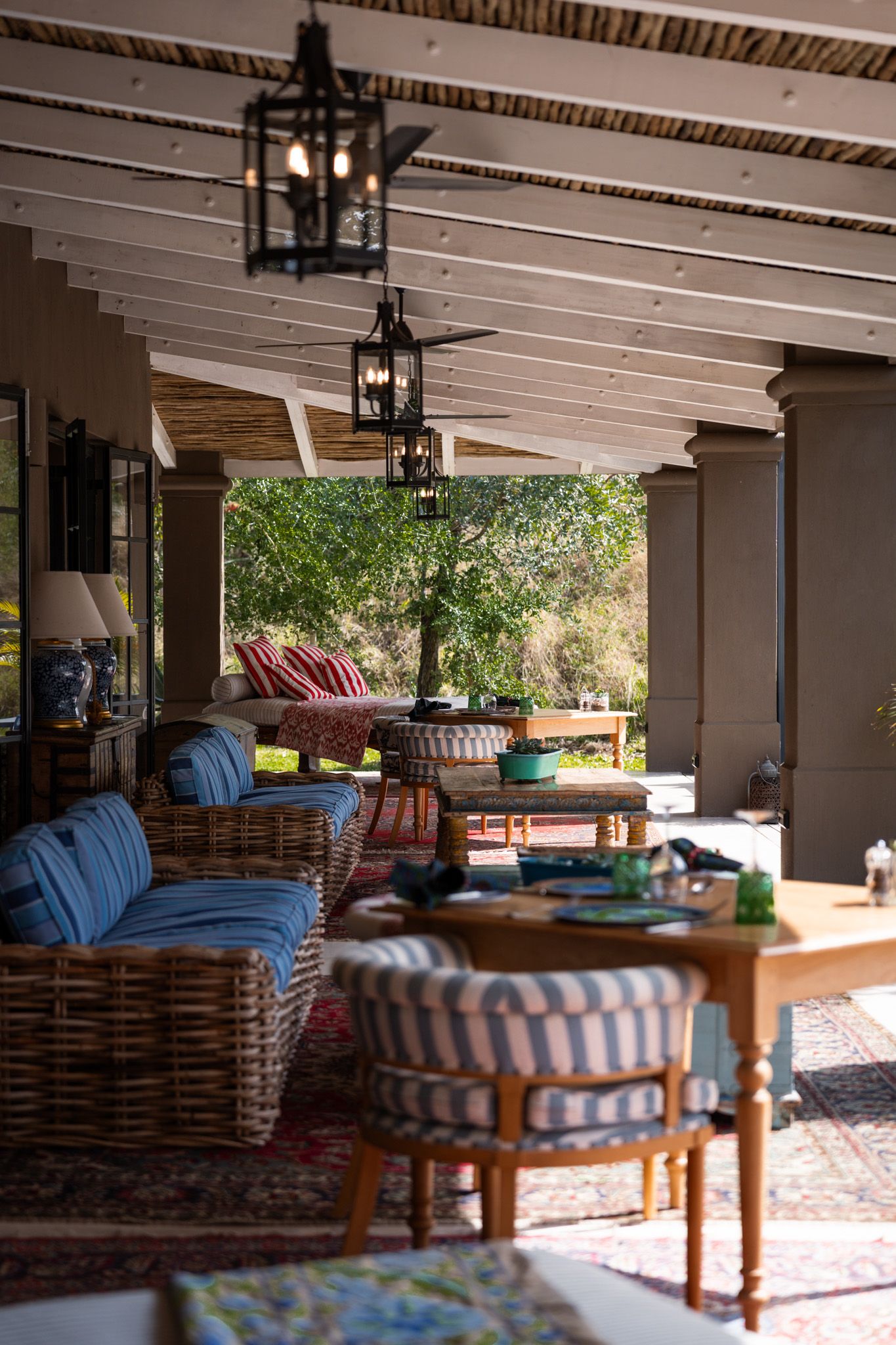 Covered outdoor lounge area with wicker furniture and striped cushions under white beamed ceiling.