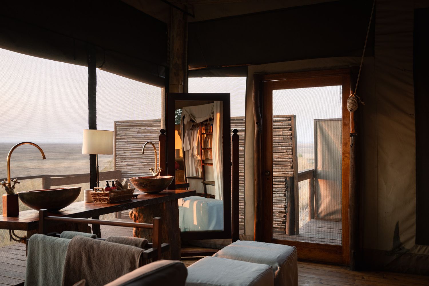 Sun-lit glamping tent interior with rustic wooden furniture and bathroom fixtures.