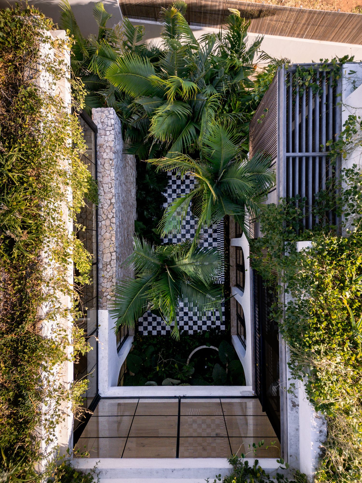Tropical garden walkway with checkered tiles and lush greenery surrounded by stone walls.