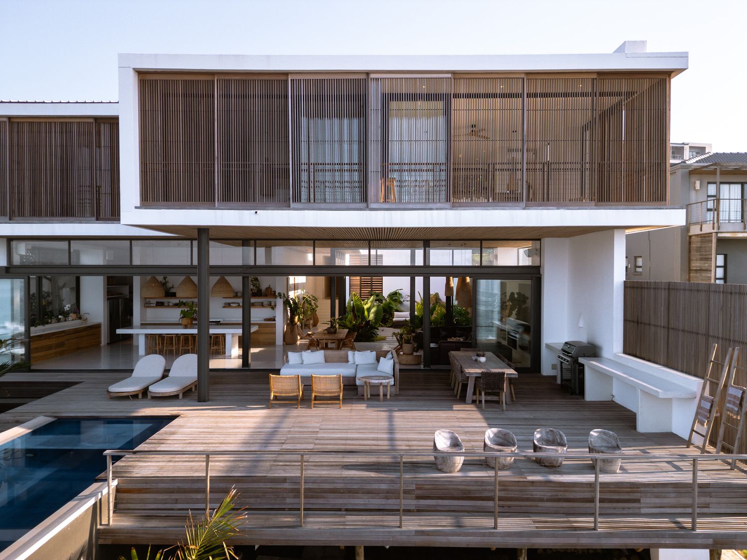 Contemporary beachfront villa with wooden facade and expansive pool deck at sunset.