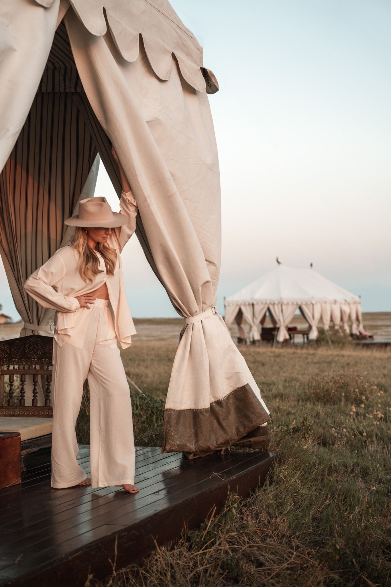 Stylish neutral-toned safari tent lodging with wooden deck in African wilderness.