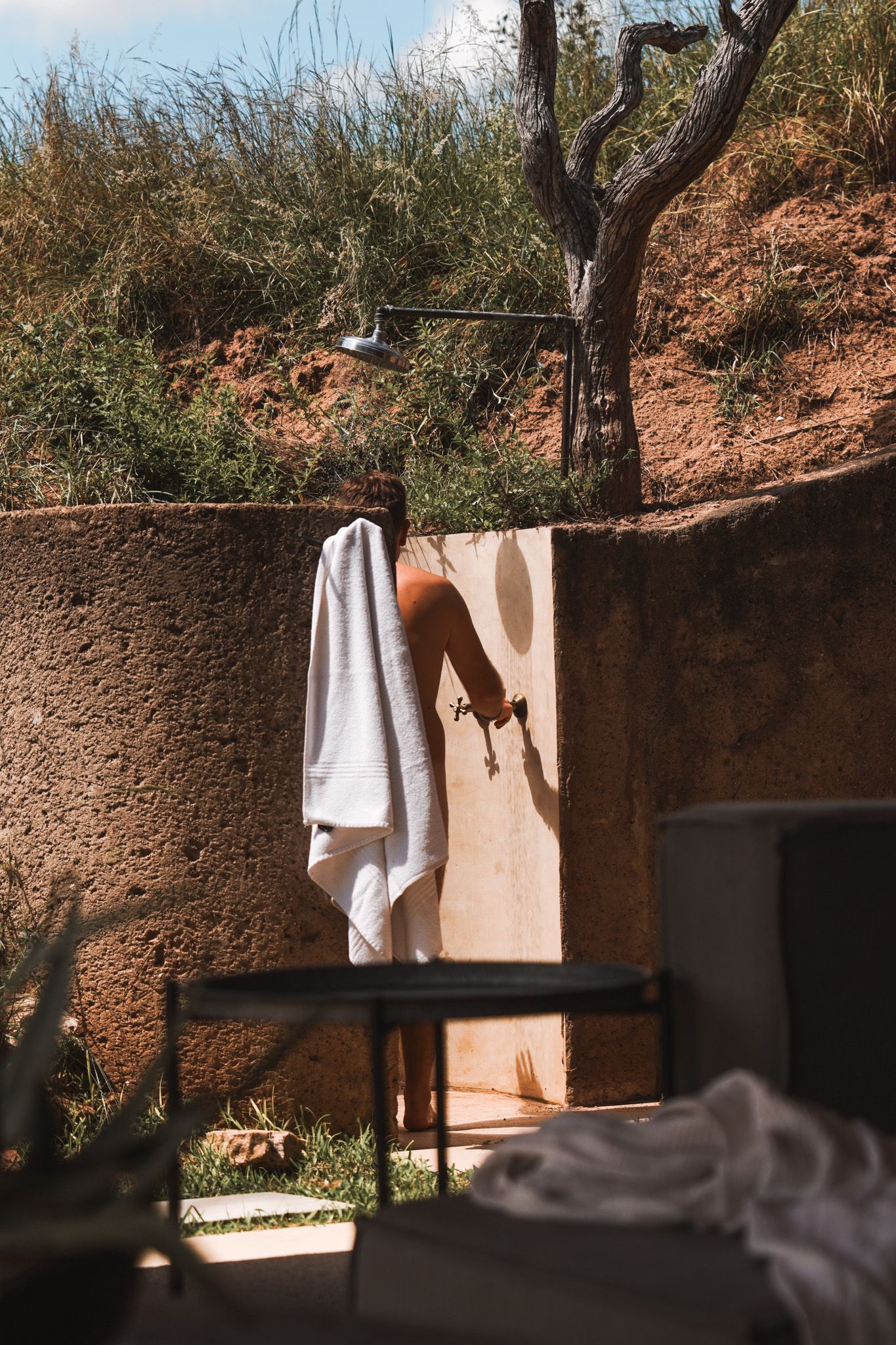 Outdoor shower area with towels hanging against an earthen wall in natural setting.