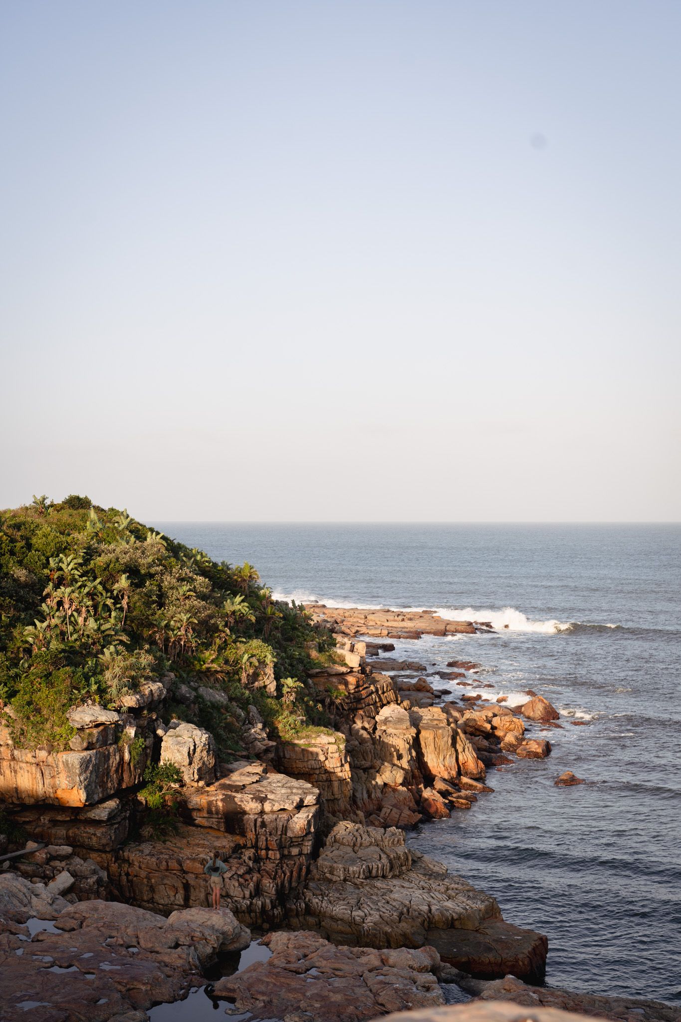 Rocky coastal cliffs meet the ocean waves under a bright sky, creating a dramatic natural seascape.