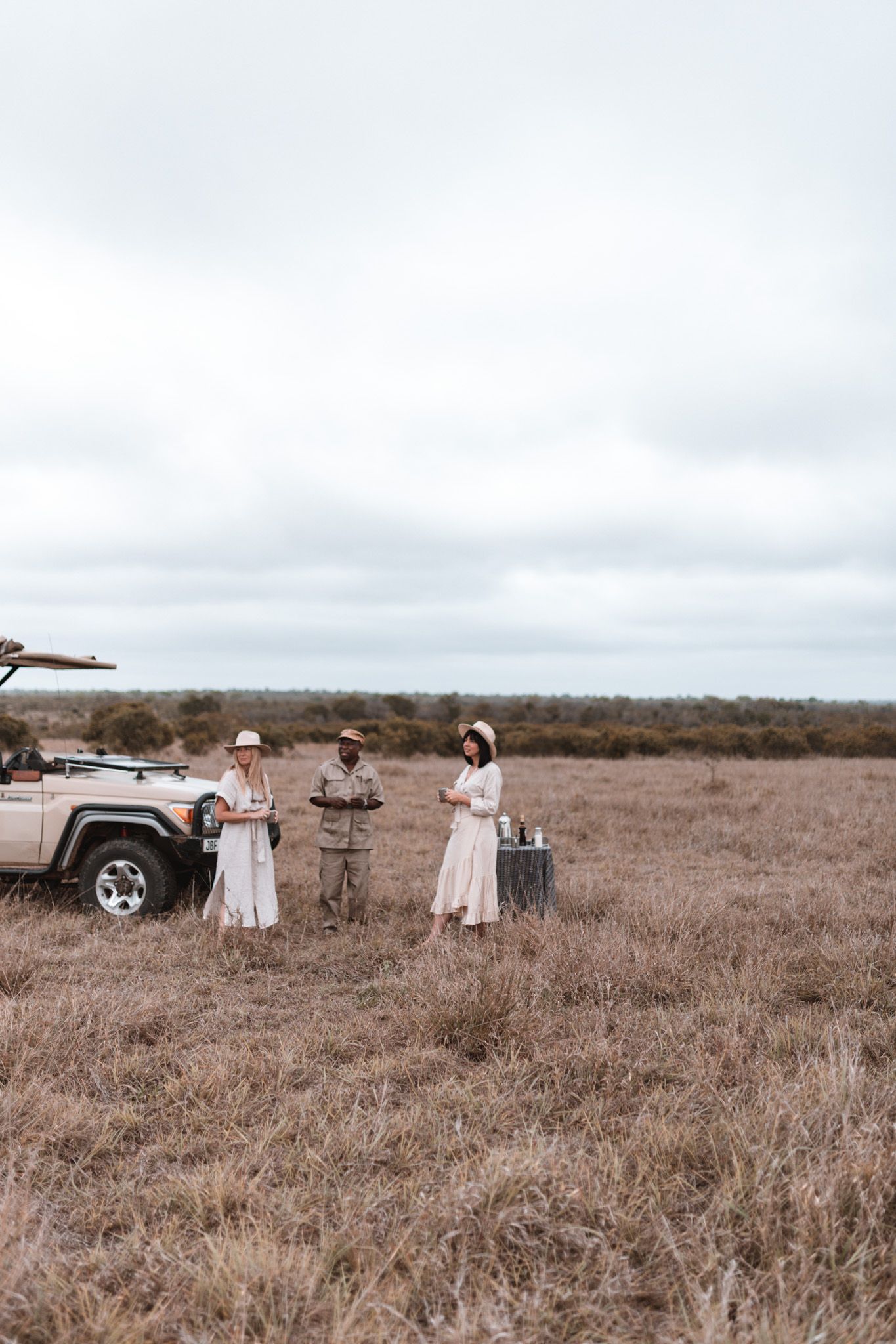 Group of travelers standing near safari vehicles in an open savanna landscape.