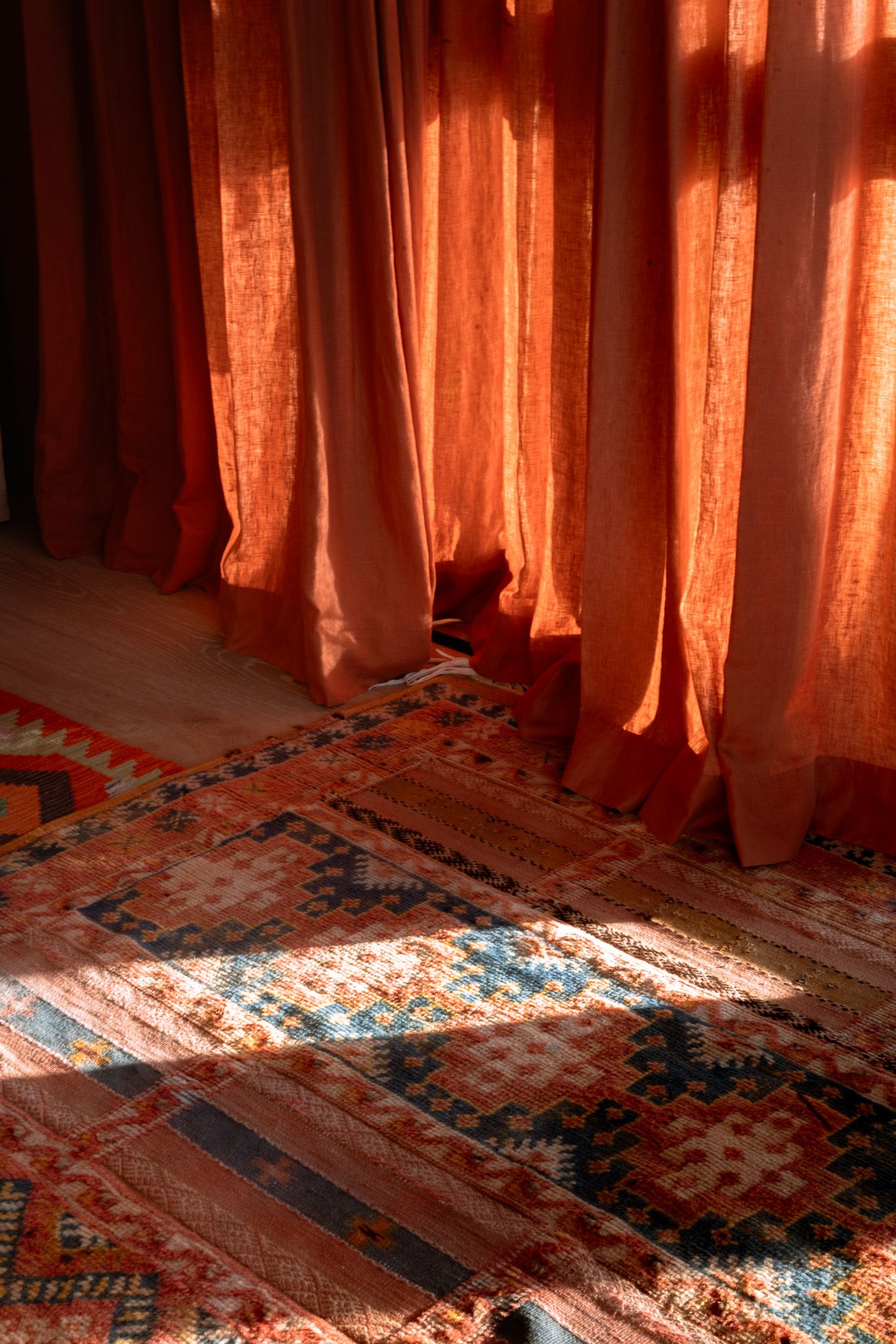 Warm sunlight streaming through orange curtains onto a patterned carpet creating geometric shadows.