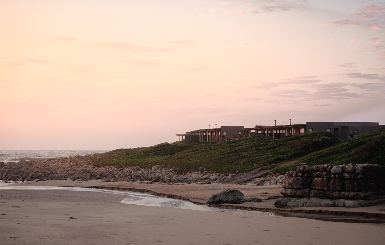 Coastal houses perched on cliffs overlooking a beach at sunset.