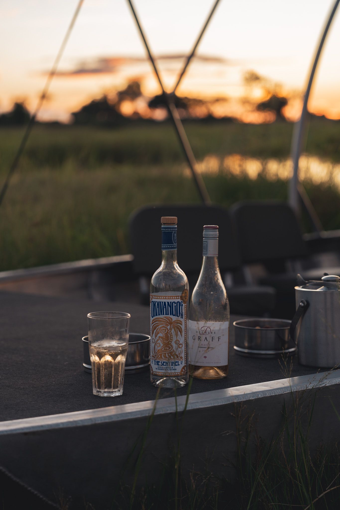 Row of beverage bottles silhouetted against a sunset sky on an outdoor surface.