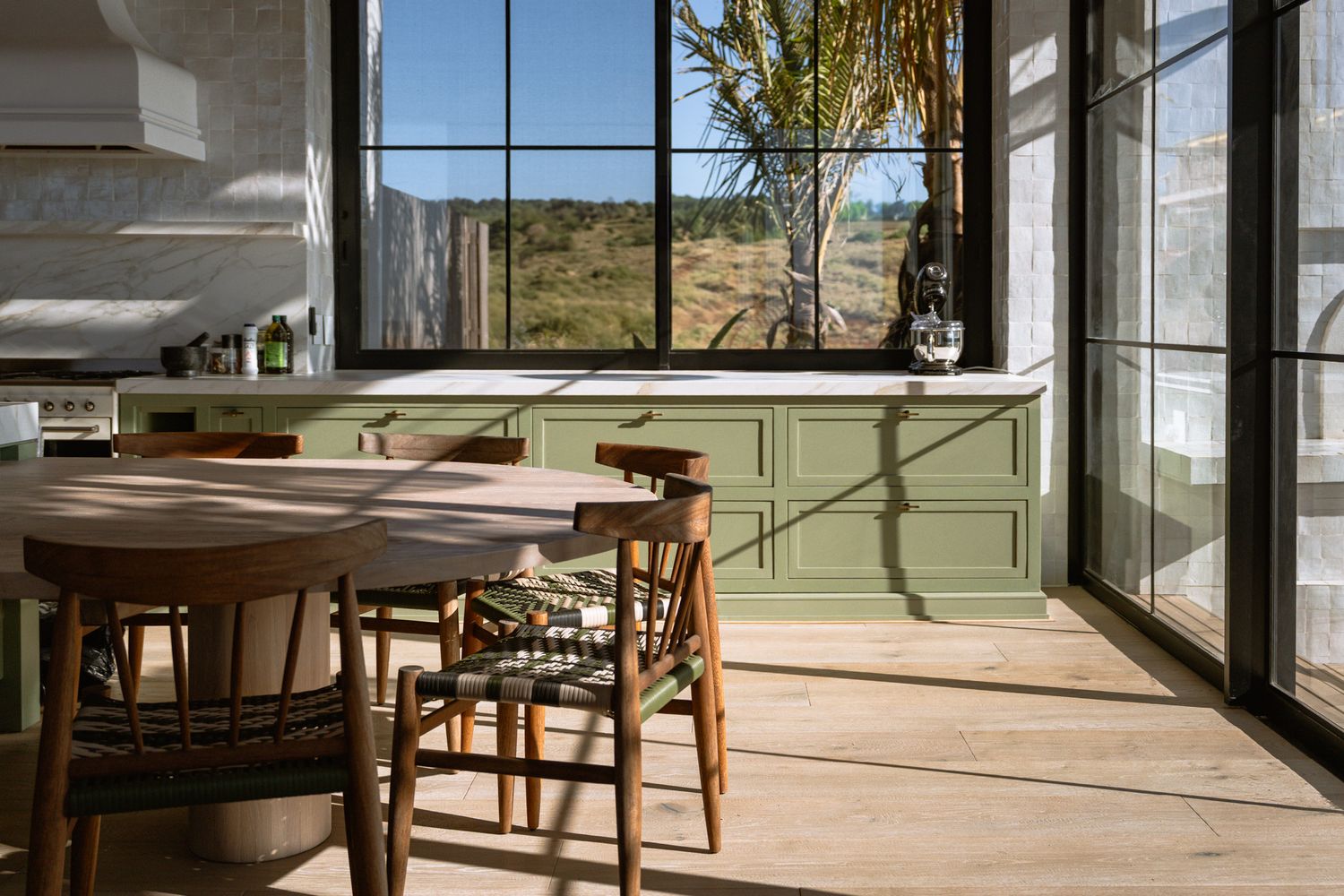 Modern dining area with wooden chairs and large windows overlooking natural landscape.