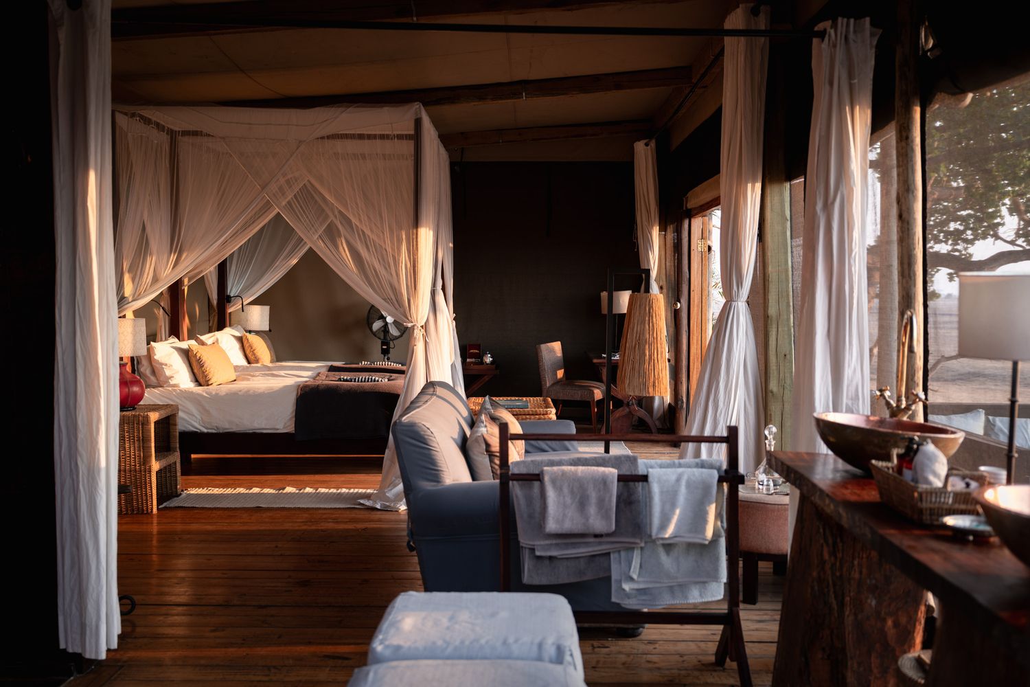 Elegant tent suite interior with canopy bed, seating area, and draped white curtains.
