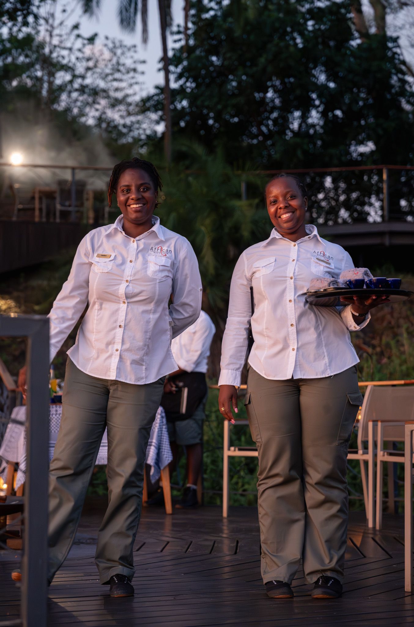 Staff members at luxury lodge carrying serving trays during evening service.