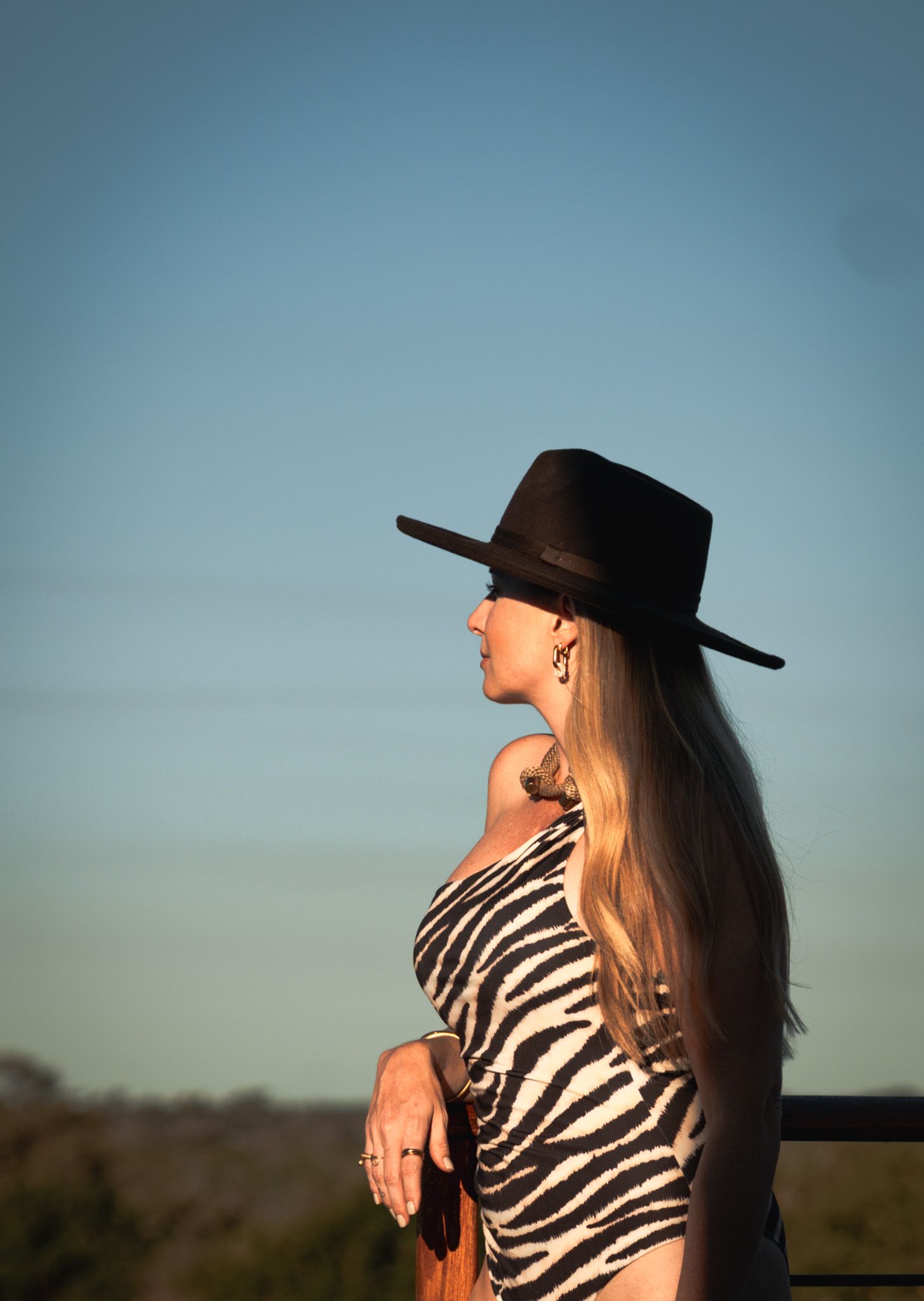Side profile portrait in zebra print and western hat against sunset sky.