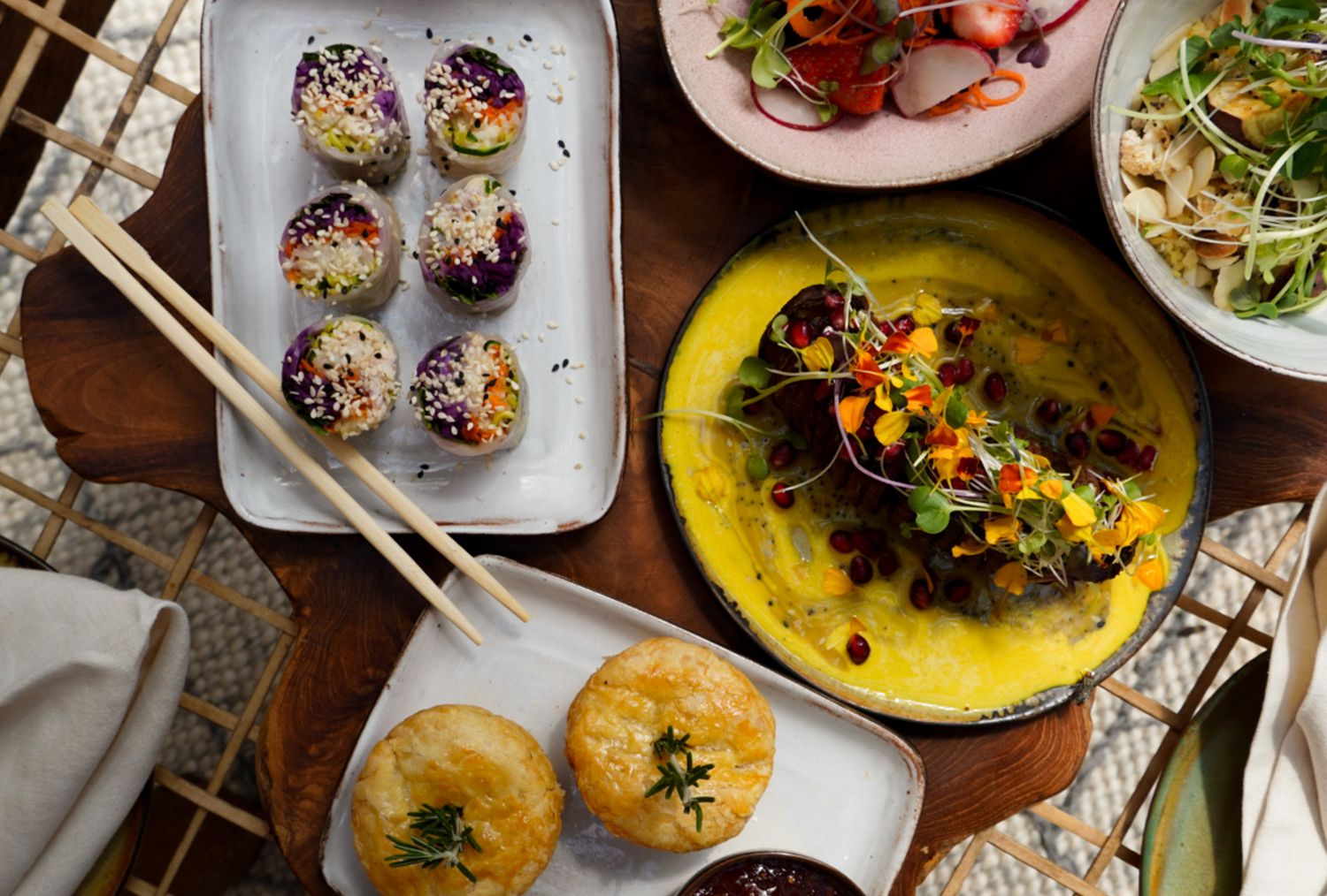 Elegant Asian fusion dishes including colorful sushi rolls and a vibrant yellow curry served on rustic wooden table.