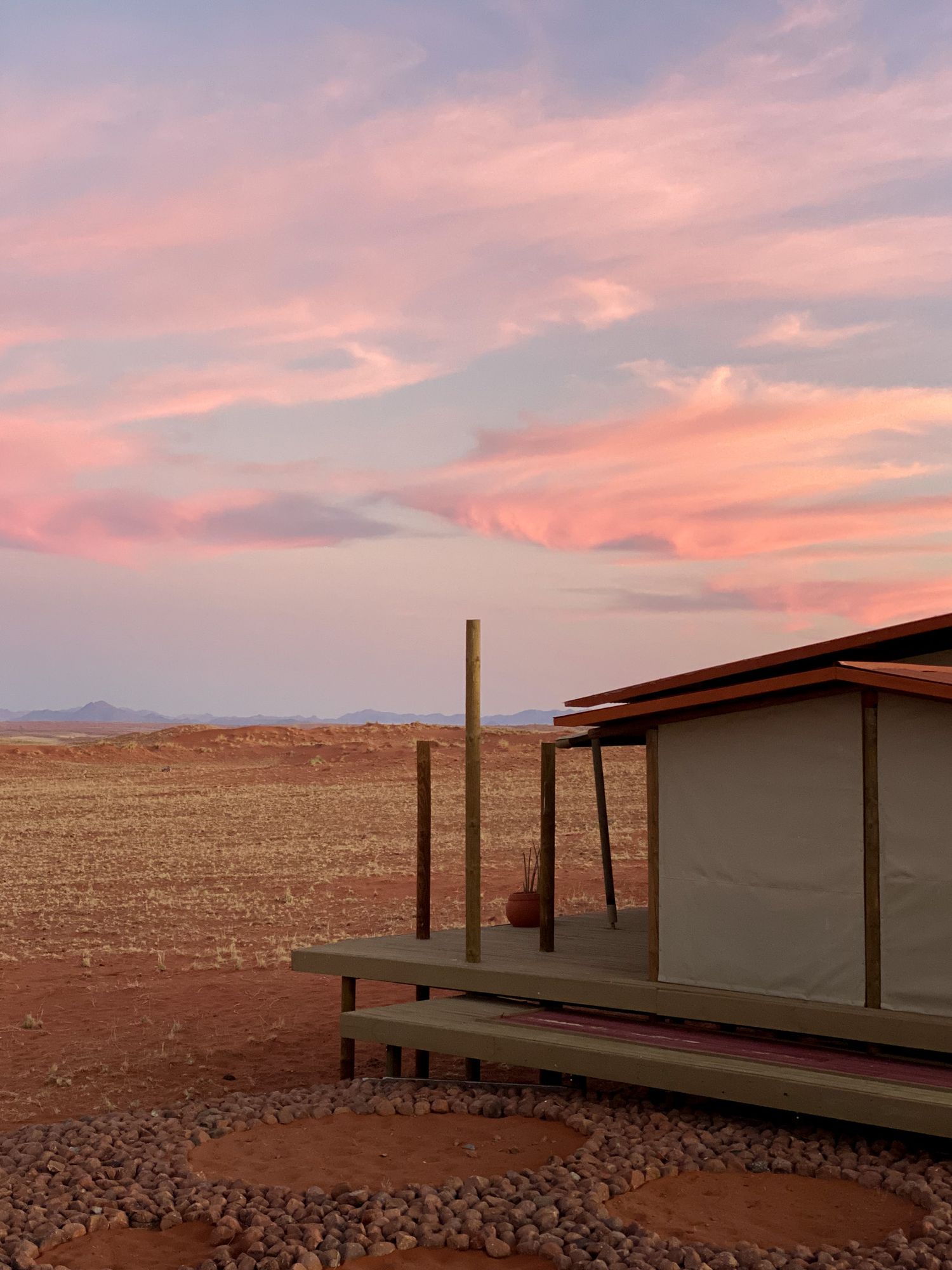 Modern desert shelter with wooden posts stands against a dramatic pink sunset sky.
