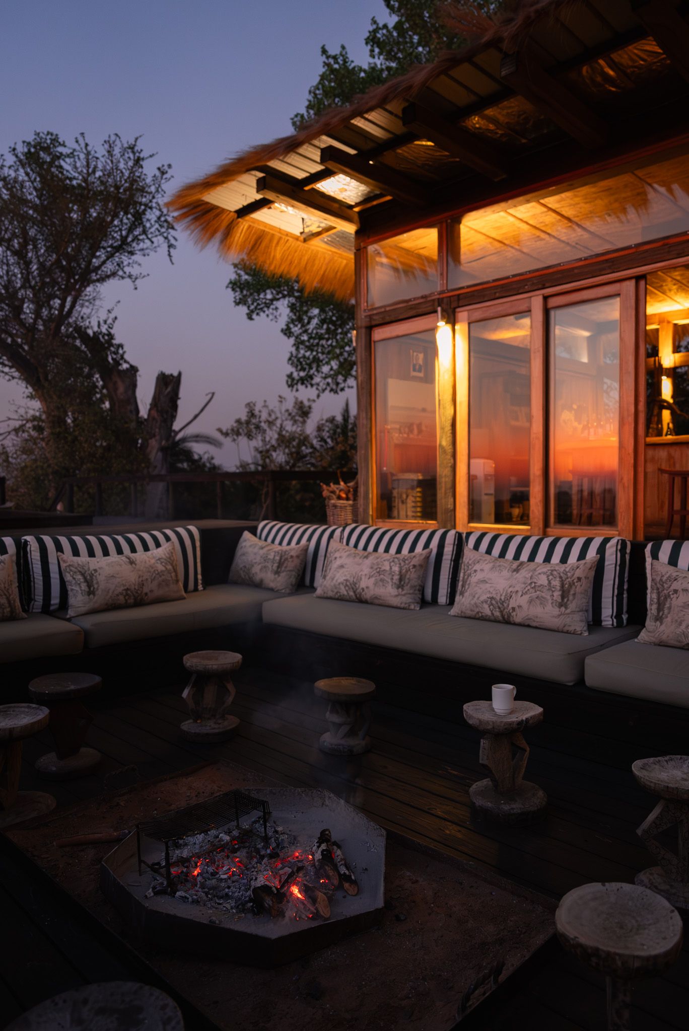 Cozy outdoor lounge area with striped cushions and fire pit glowing at sunset.