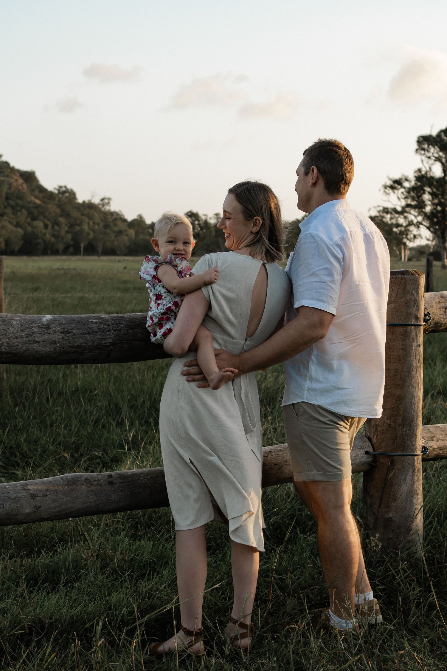 A family shares a tender moment while leaning against a wooden fence at sunset.
