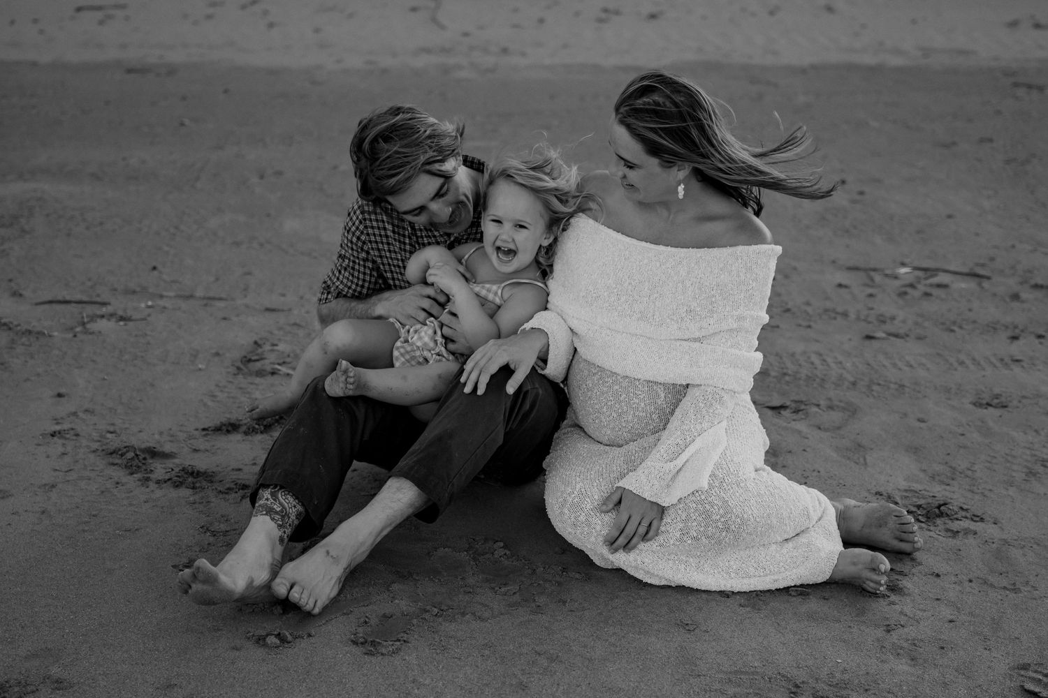A black and white image of a family sharing an intimate moment on the beach.