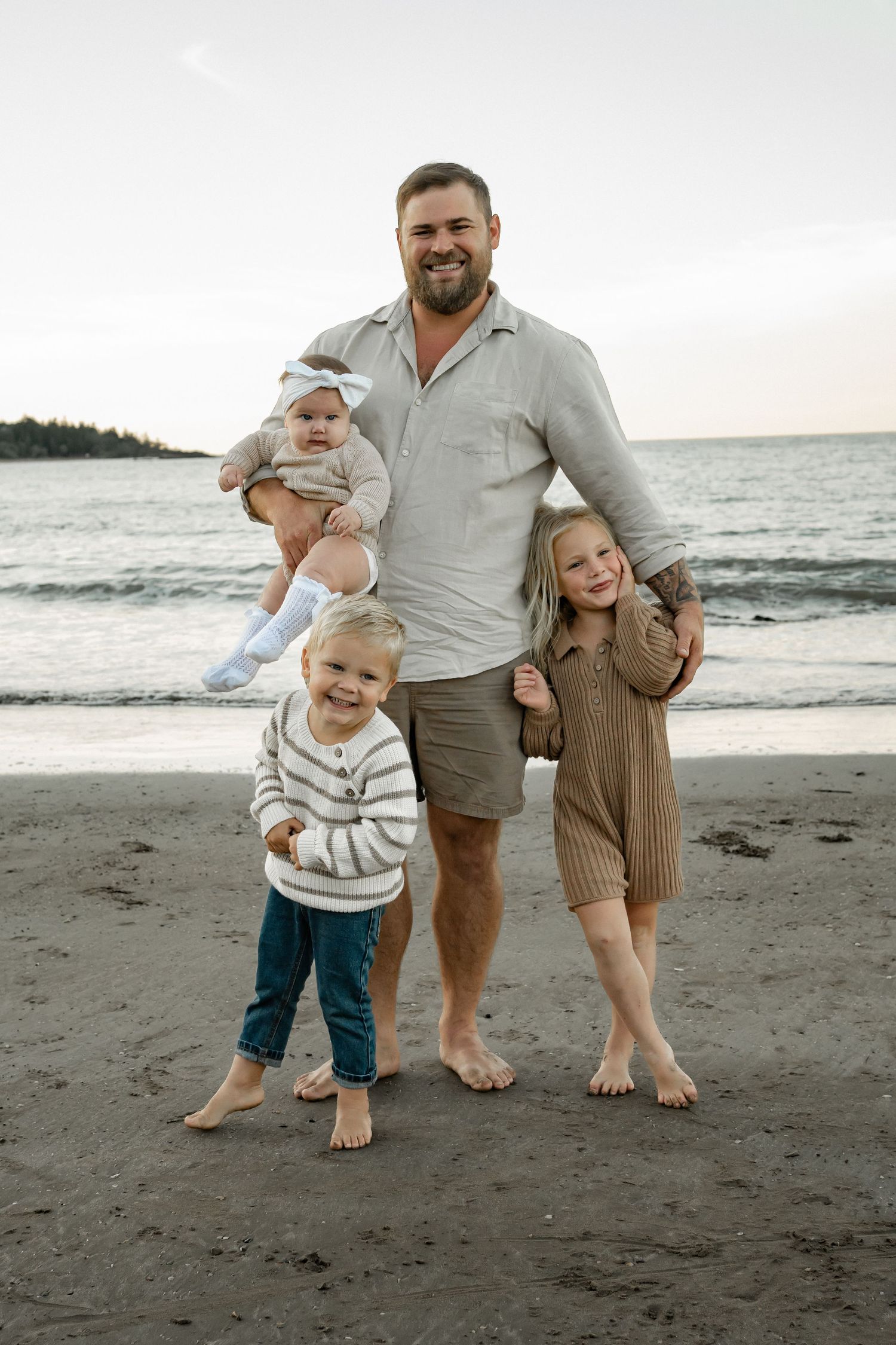 Family enjoying a barefoot walk together on a black sand beach at sunset.