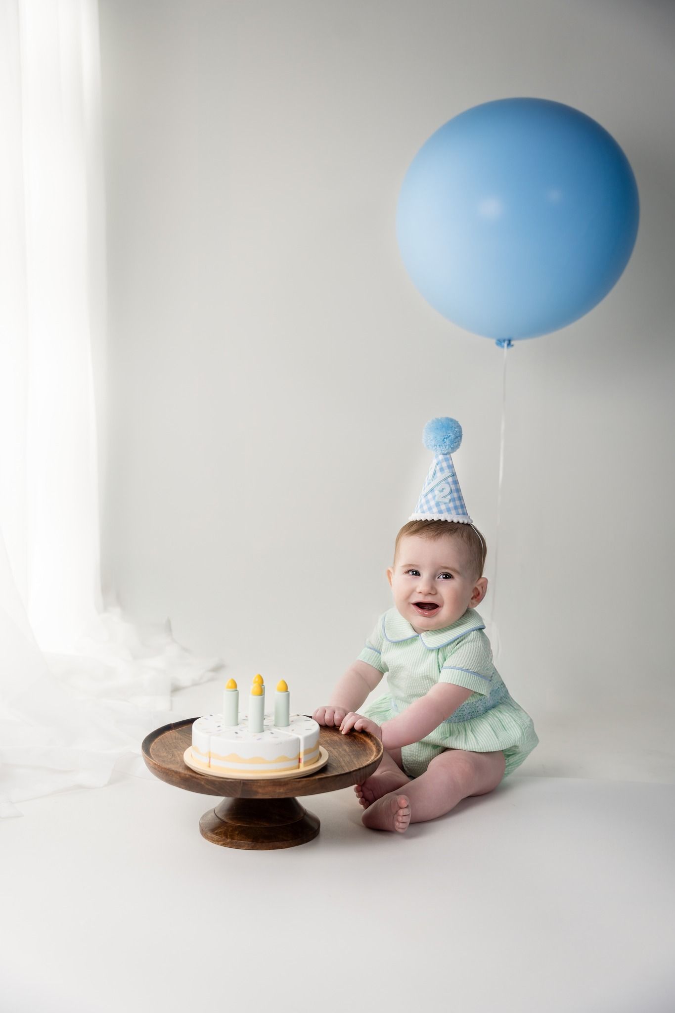 Birthday setup with blue balloon and wooden cake stand against white background.