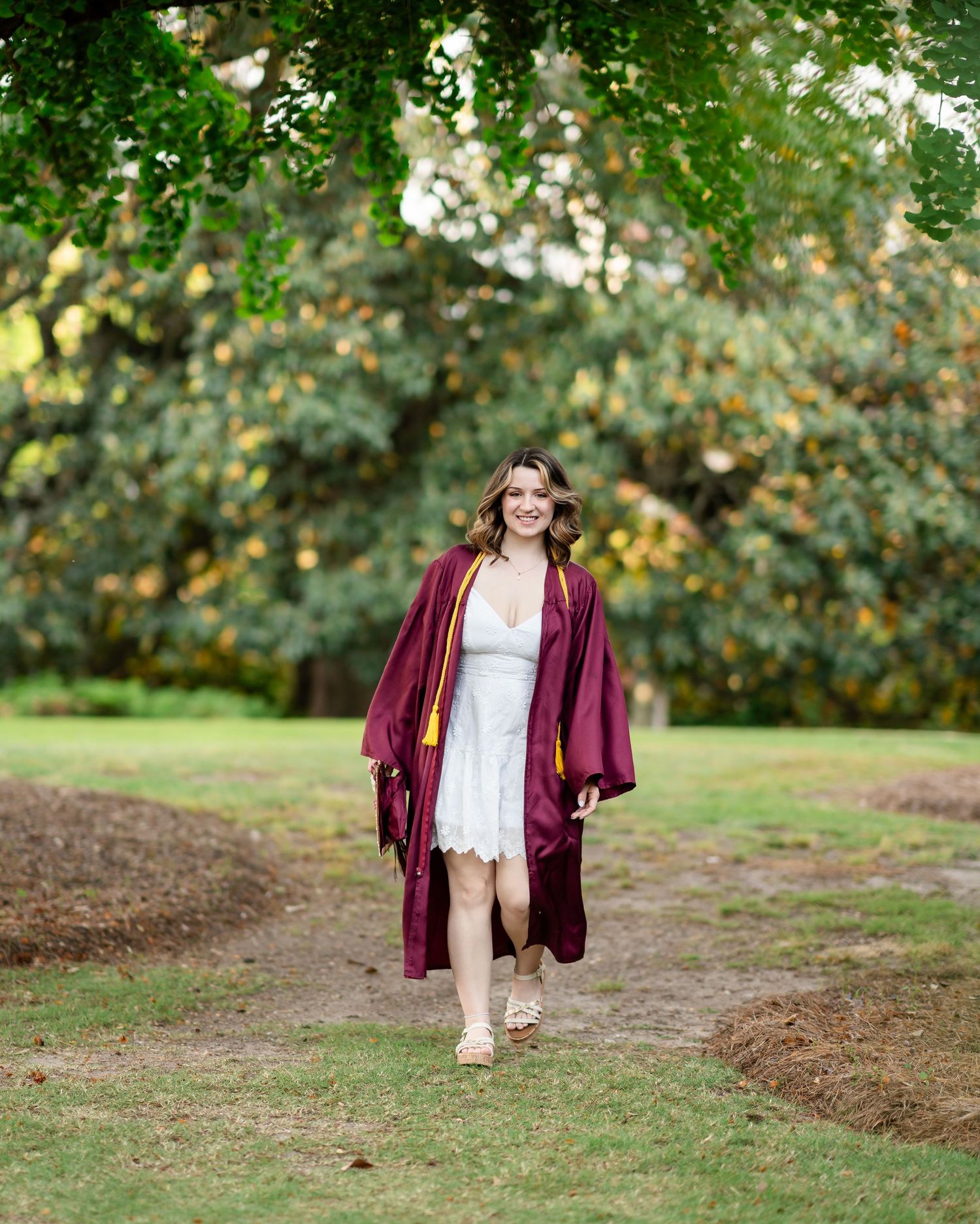 A burgundy graduation gown flows in a playful series of outdoor portraits against a lush green background.