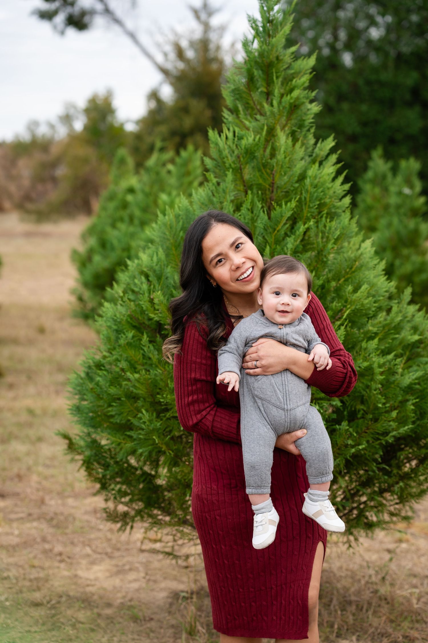 A candid moment captured at a Christmas tree farm with festive burgundy sweater against evergreen trees.