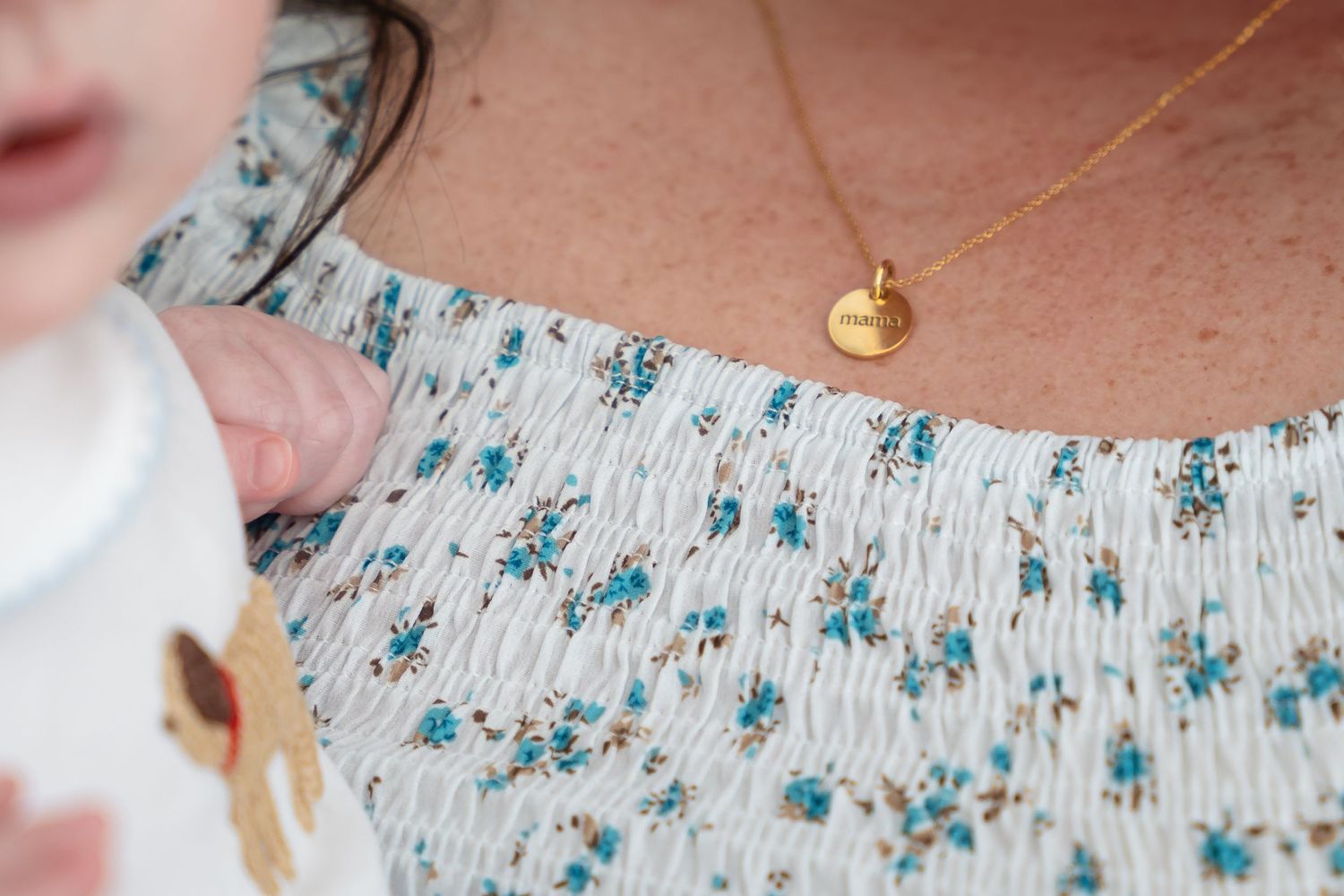 Close-up detail of a delicate blue floral pattern on a white dress with a gold necklace.