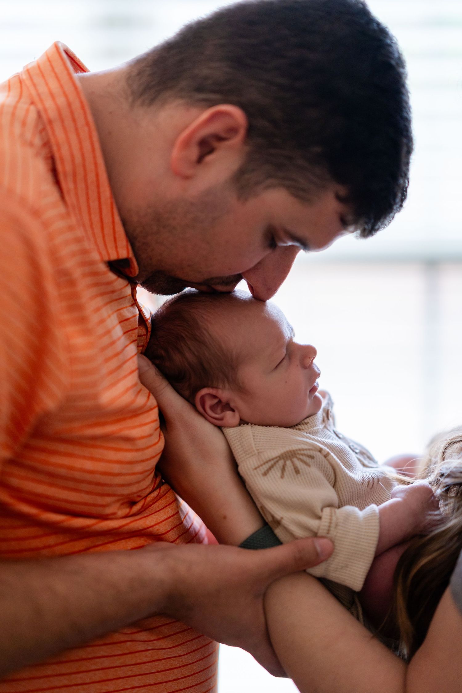 Parent in orange shirt tenderly kissing newborn baby.