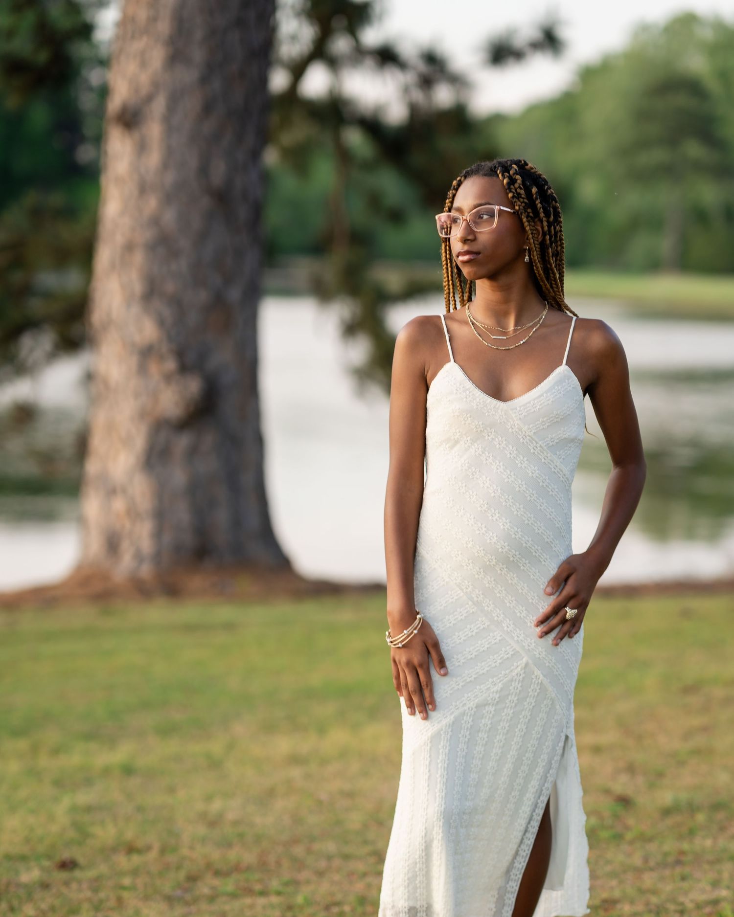 Portrait session in white dress among tall pine trees near a lake.