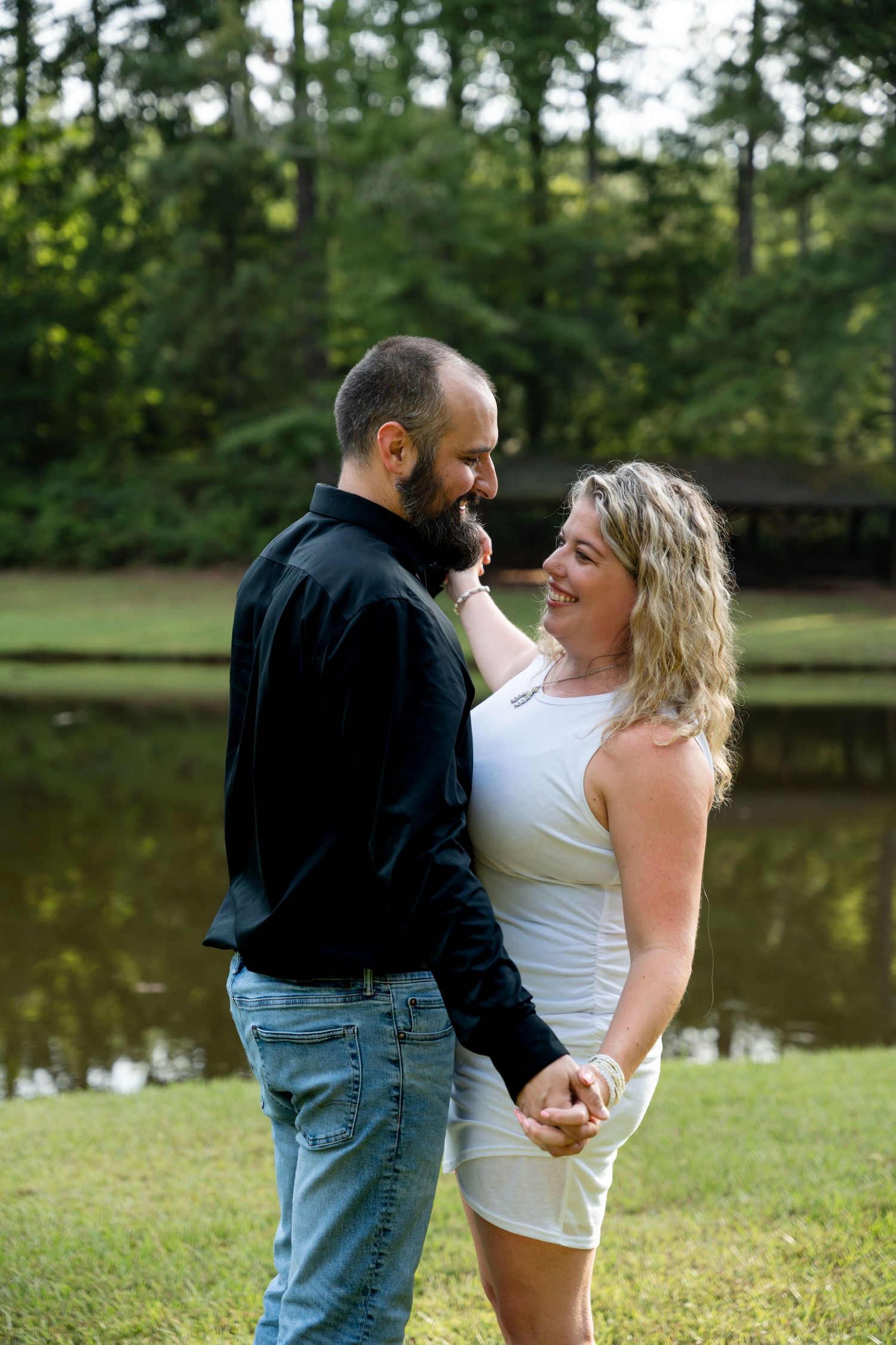 Couple holding hands and smiling at each other near peaceful lake.