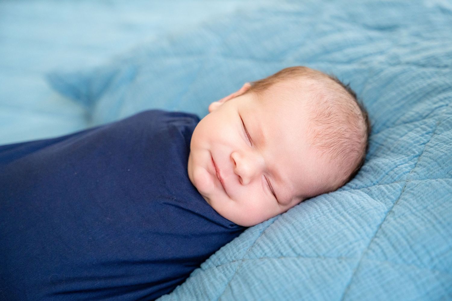 Newborn baby sleeping peacefully on light blue bedding.