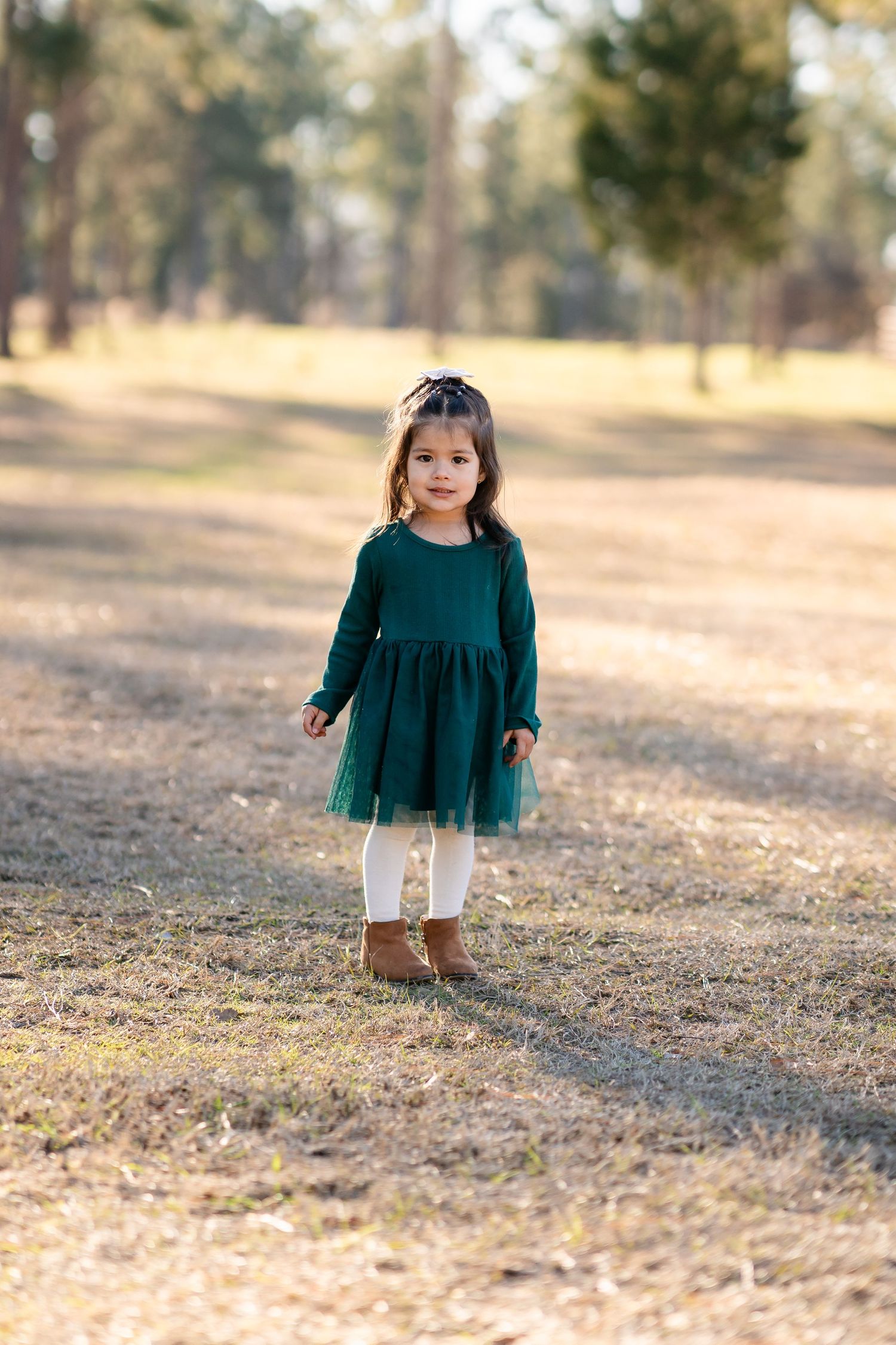 Small child in emerald green dress walking through fallen leaves in a park.