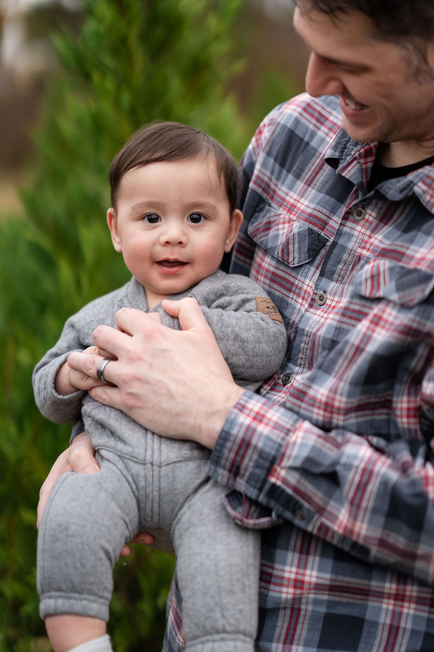 Sweet interaction with a baby wearing grey clothes against an outdoor backdrop.